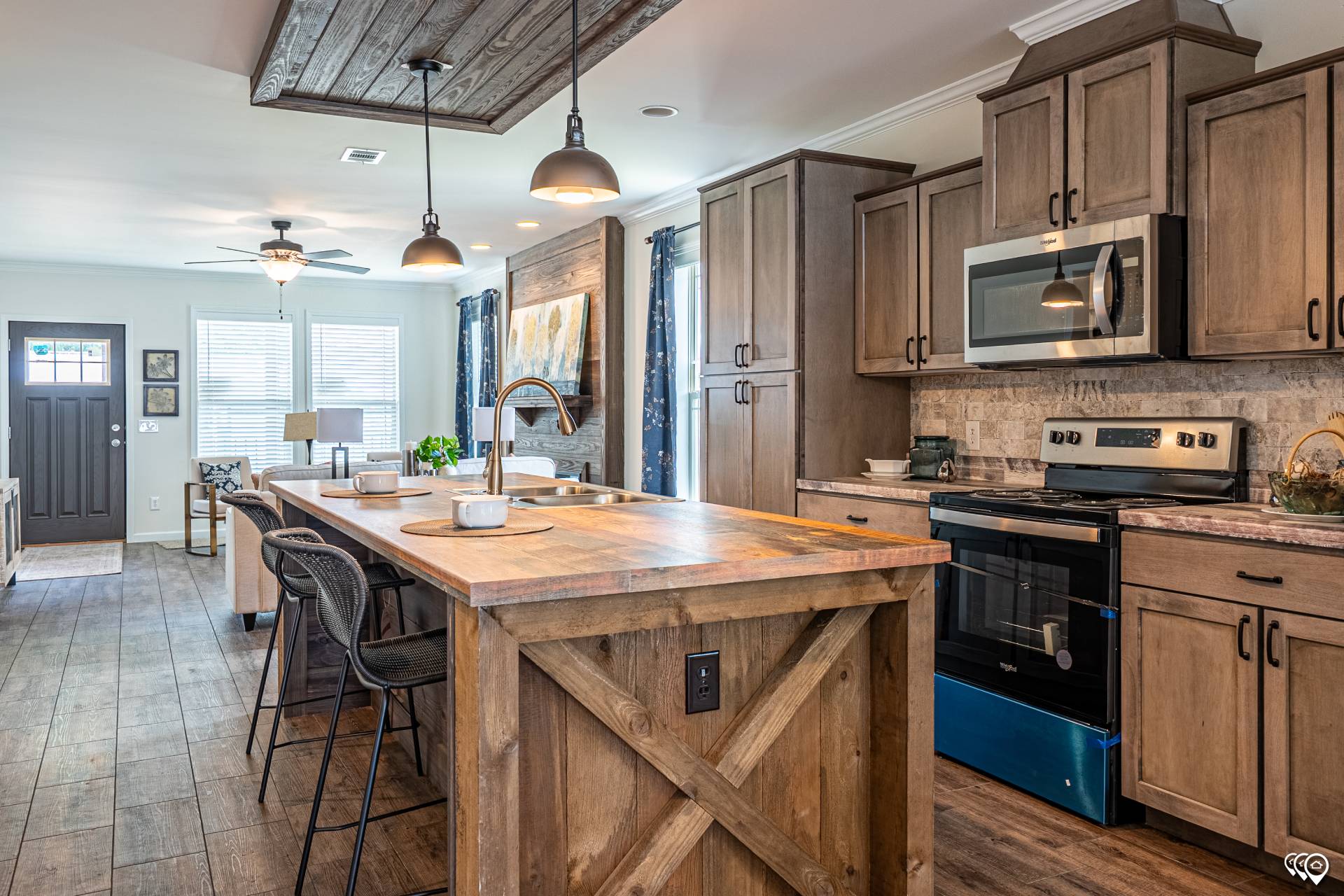 Rustic kitchen and dining area with wooden cabinets, island, and flooring. Overhead lights create a warm ambiance. Open, airy feel with natural light.
