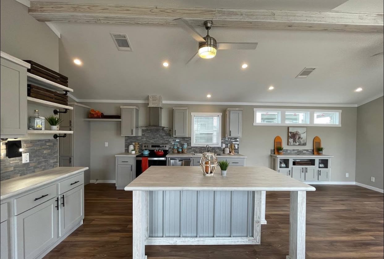 Modern kitchen with open layout, featuring wood floors, gray cabinetry, a central island, stainless appliances, and warm recessed lighting.