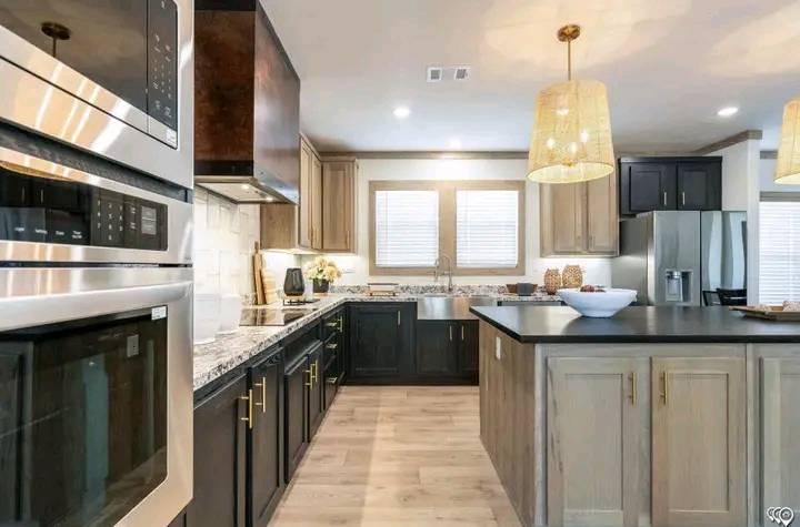 Modern kitchen with stainless steel appliances, light wood flooring, and dark and light cabinetry. Pendant lights add warmth and elegance.
