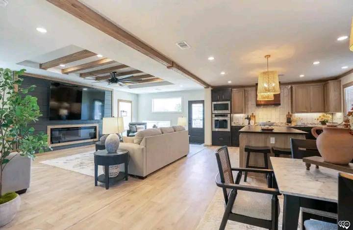 Spacious open-plan living area featuring light wood floors, a modern kitchen with island, cozy lounge with sectional sofa, and warm lighting accents.