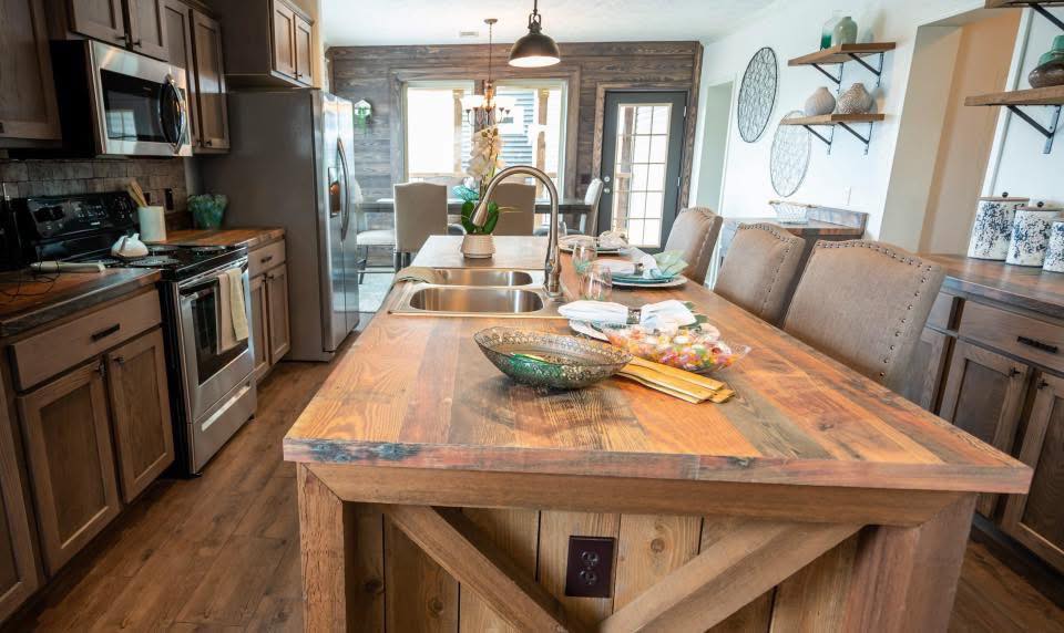 Rustic kitchen with wooden cabinets and island, modern appliances, and decorative shelves. Soft lighting adds warmth and a cozy, inviting atmosphere.