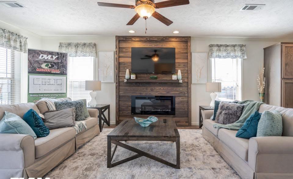 A cozy living room with beige sofas adorned with blue and gray pillows, a large wooden coffee table, and a wall-mounted TV above an electric fireplace.