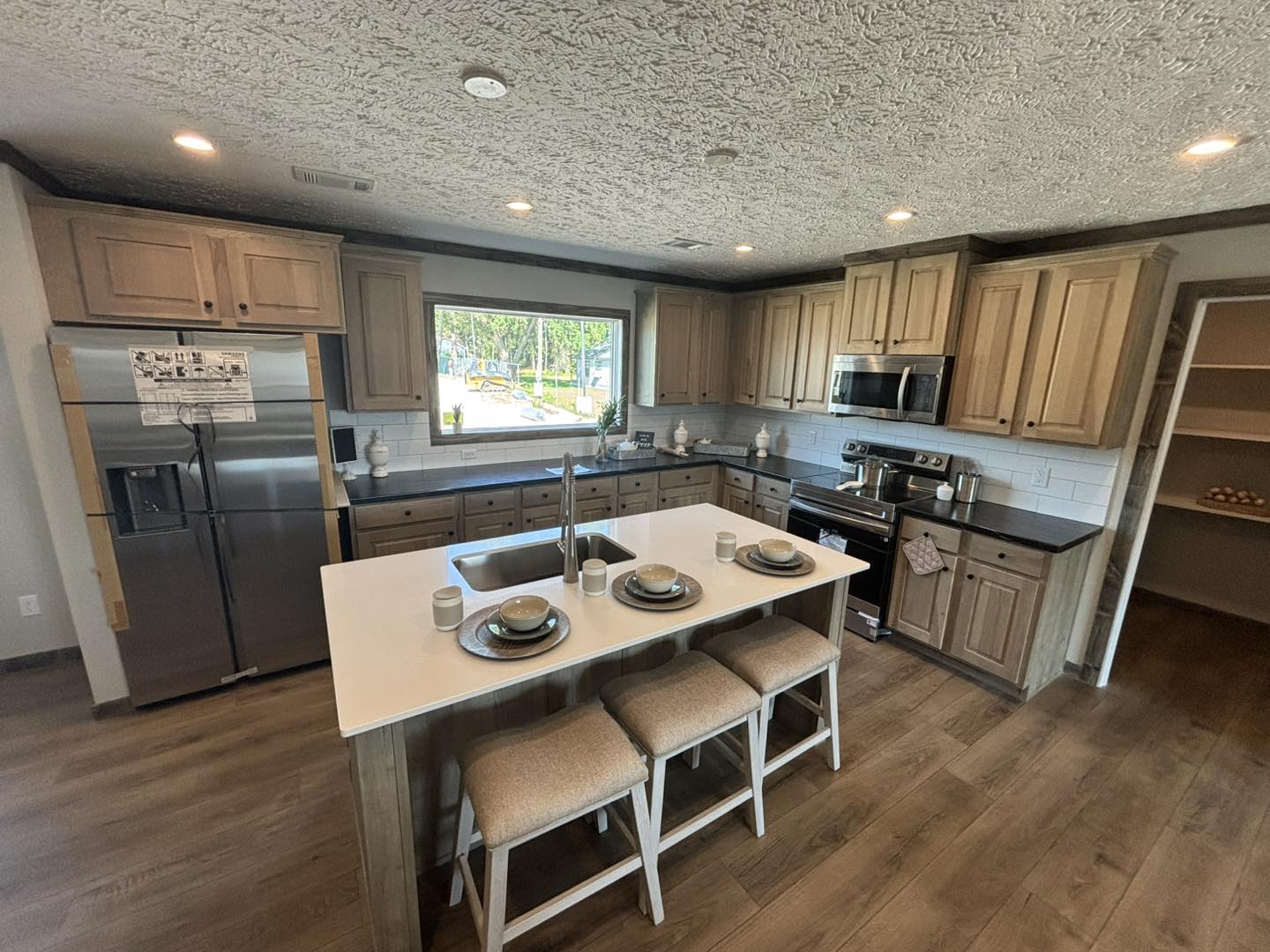 Modern kitchen with wooden cabinets, stainless steel appliances, and a large island featuring place settings. A bright, airy feel with natural light from a window.