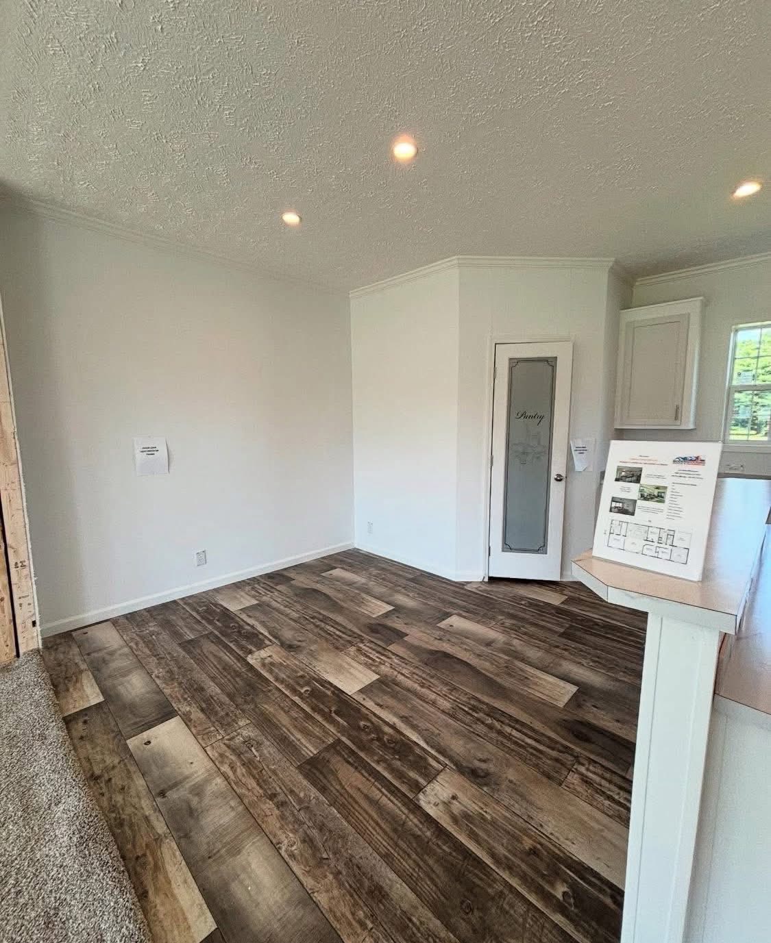 Spacious room with white walls, wood-patterned flooring, and a glass panel door labeled "Pantry." Recessed lighting creates a bright, inviting atmosphere.