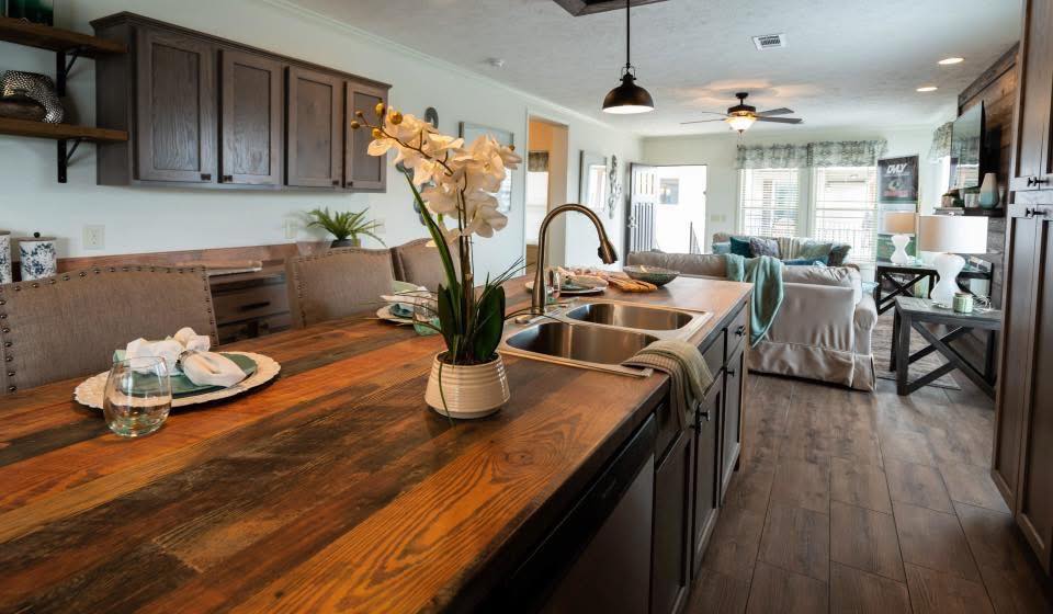 Rustic kitchen and living area with wooden island, elegant orchid centerpiece, cozy seating, wooden cabinets, and warm lighting, creating a welcoming vibe.