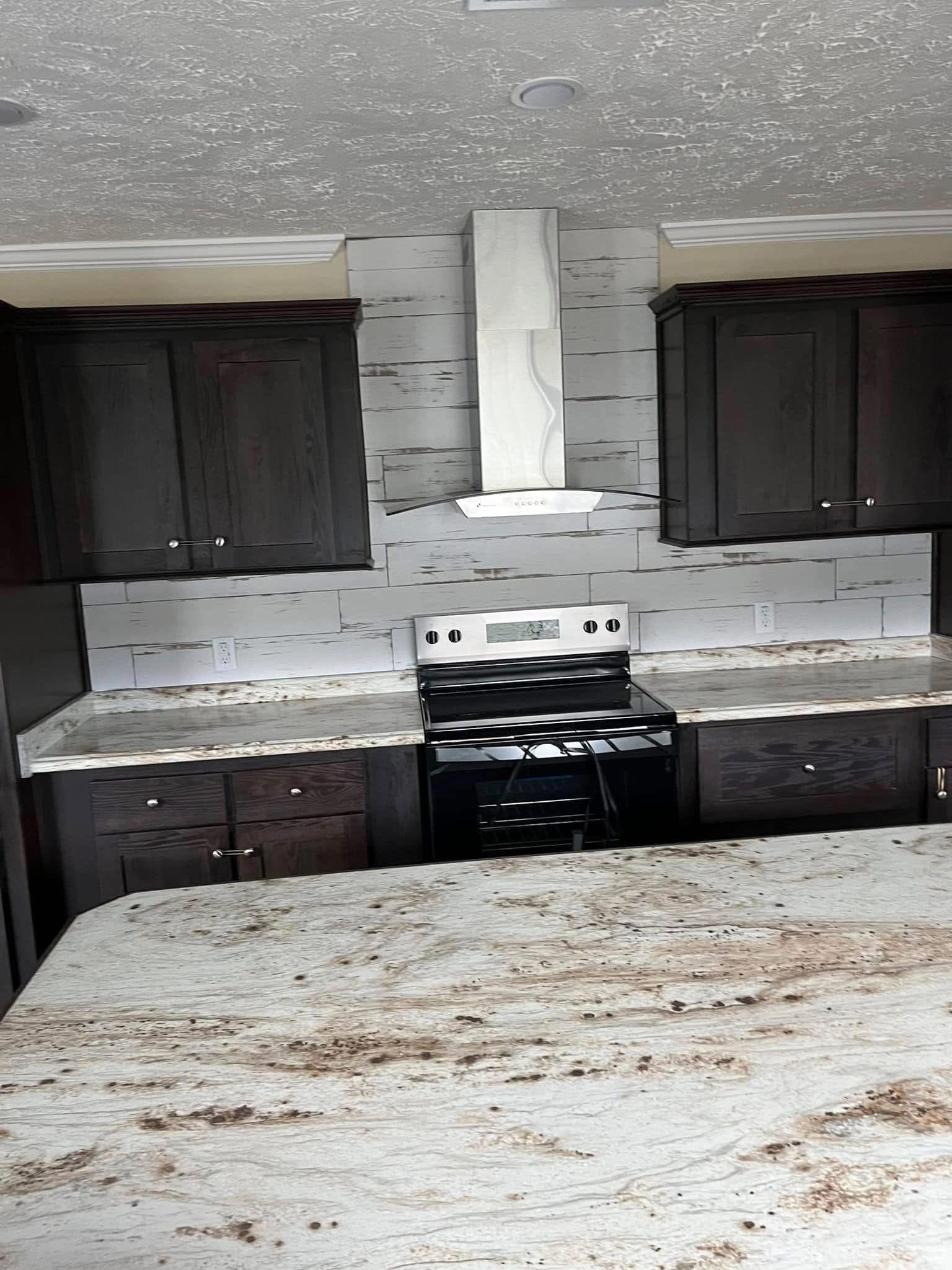 Modern kitchen with dark wood cabinets, white marbled countertops, and a central stove. The backsplash features light wood paneling, creating a sleek, contemporary feel.