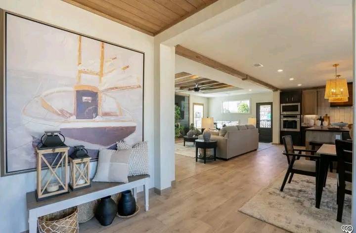 Warm, inviting living space with a boat painting and bench in the entry. Open floor plan leads to a cozy kitchen and living room, featuring wood accents and soft lighting.
