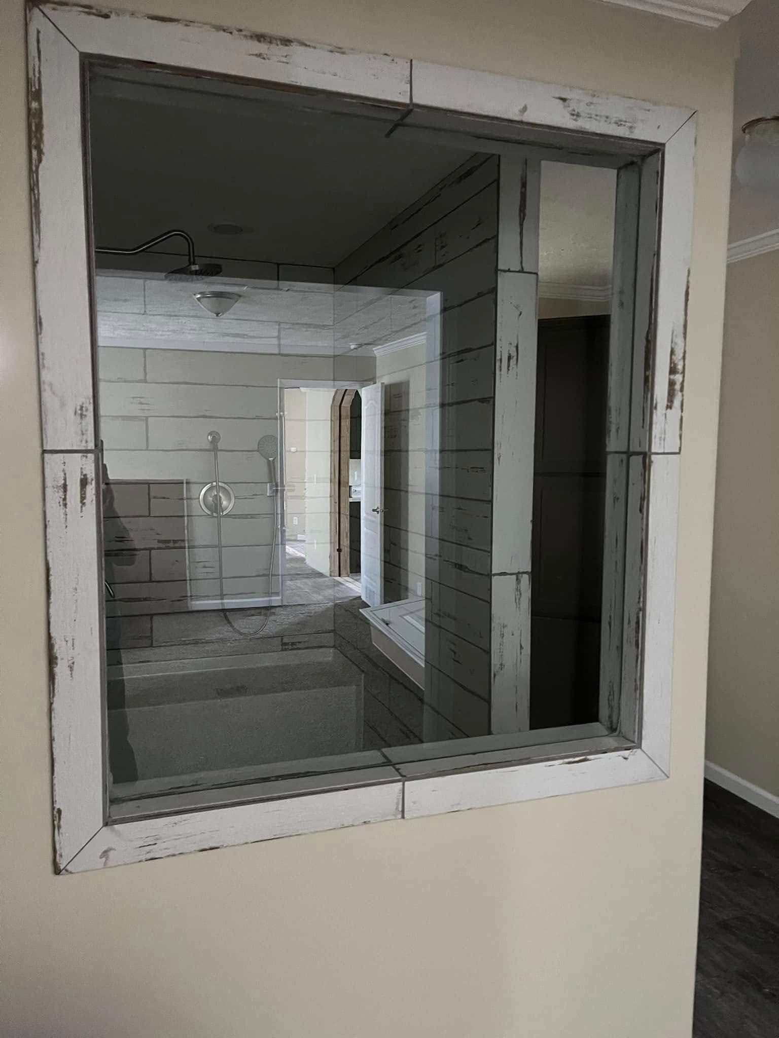 Reflection of a shower room in a distressed white-framed mirror, creating an illusion of a window to another space. Warm, rustic ambiance.