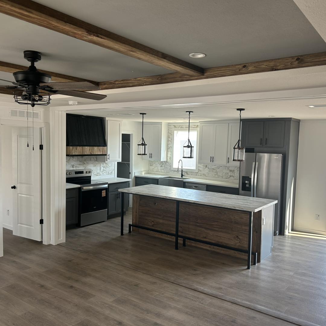 Spacious kitchen with a modern design features an island with wood paneling, white cabinets, marble backsplash, pendant lights, and wood beam ceiling accents.