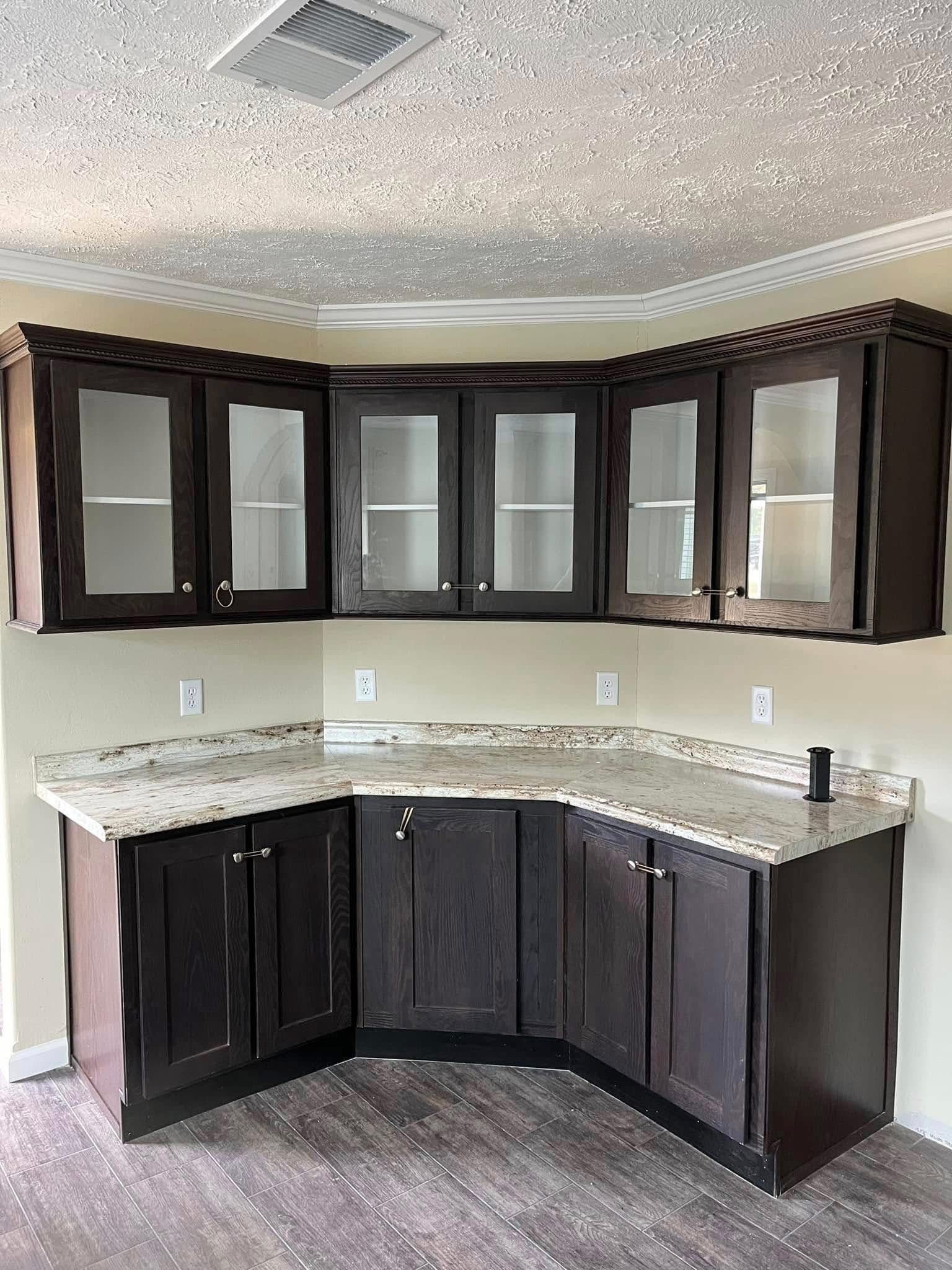 Dark wood kitchen cabinets with glass doors are set against a light beige wall. Marble countertops and a wood floor create a modern, inviting space.