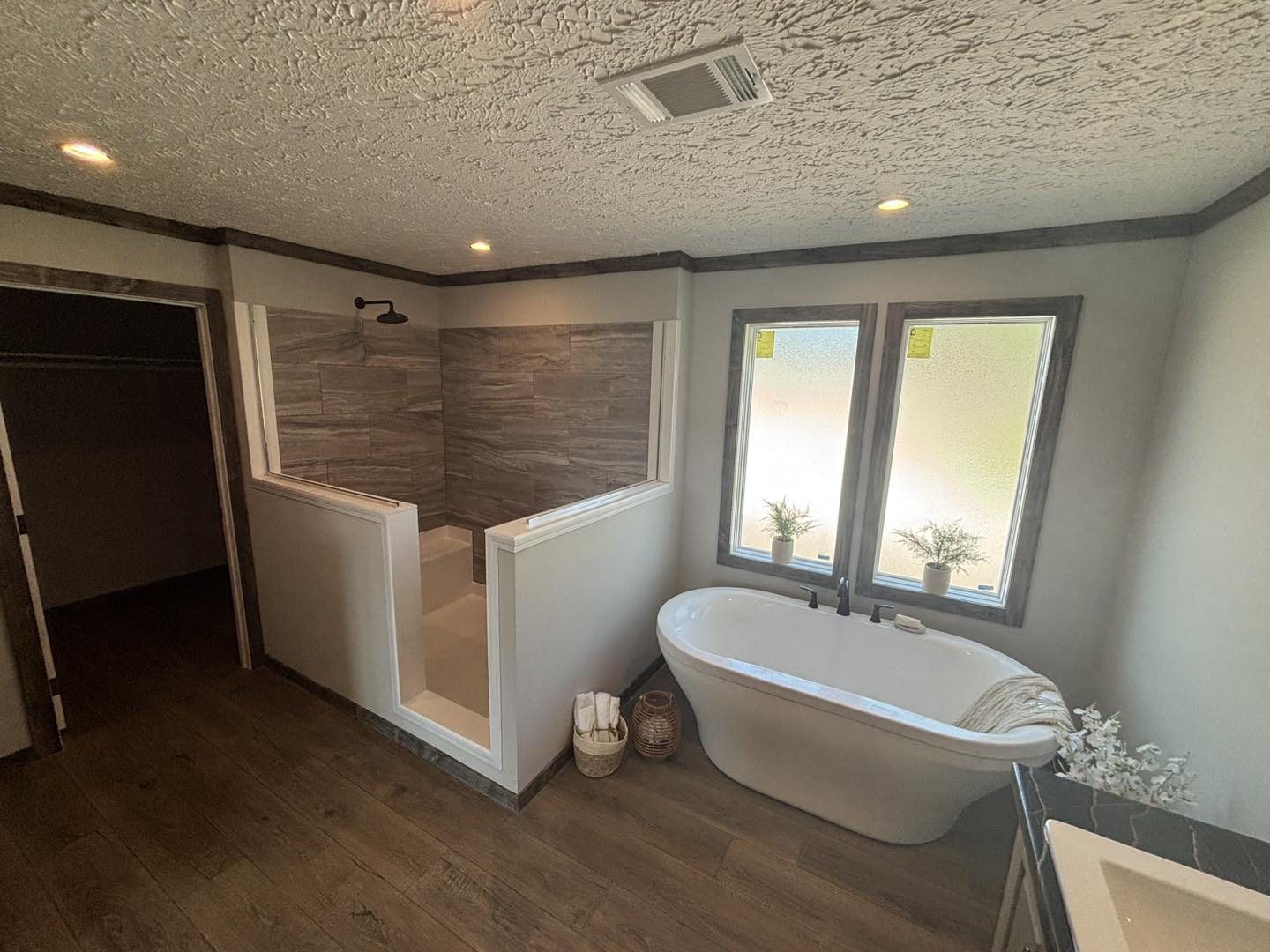 Spacious bathroom with a freestanding white bathtub under two frosted windows. Adjacent is a walk-in shower with gray tile walls. Warm and inviting.