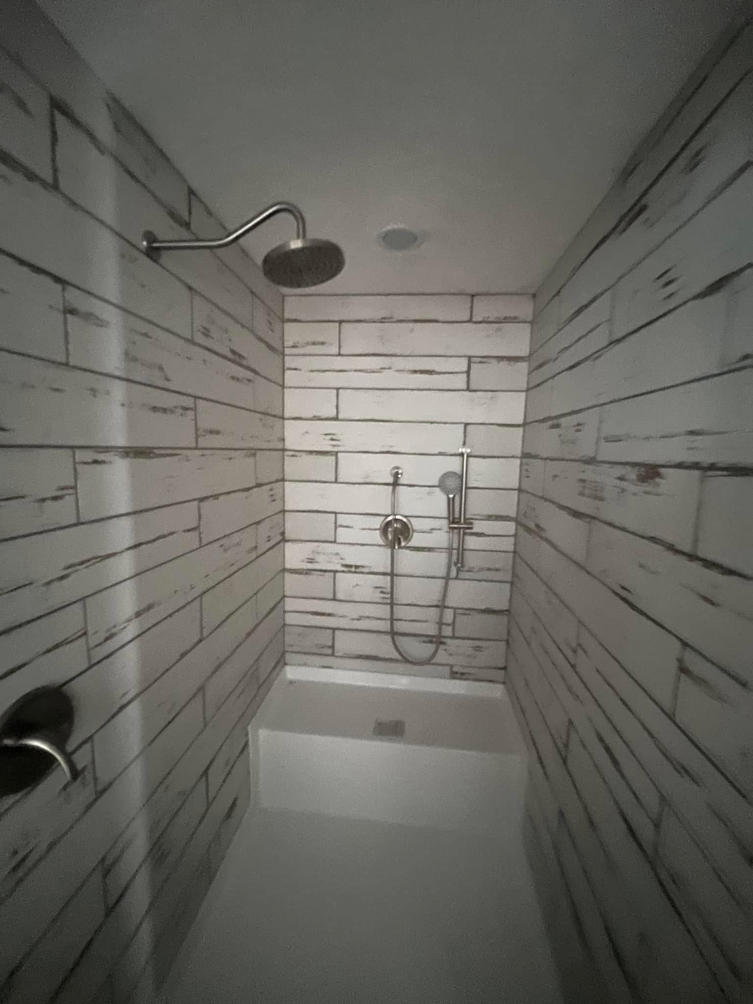 Narrow shower with white wooden plank walls, silver showerhead, and handheld nozzle. Minimalist and rustic with a clean, modern feel.
