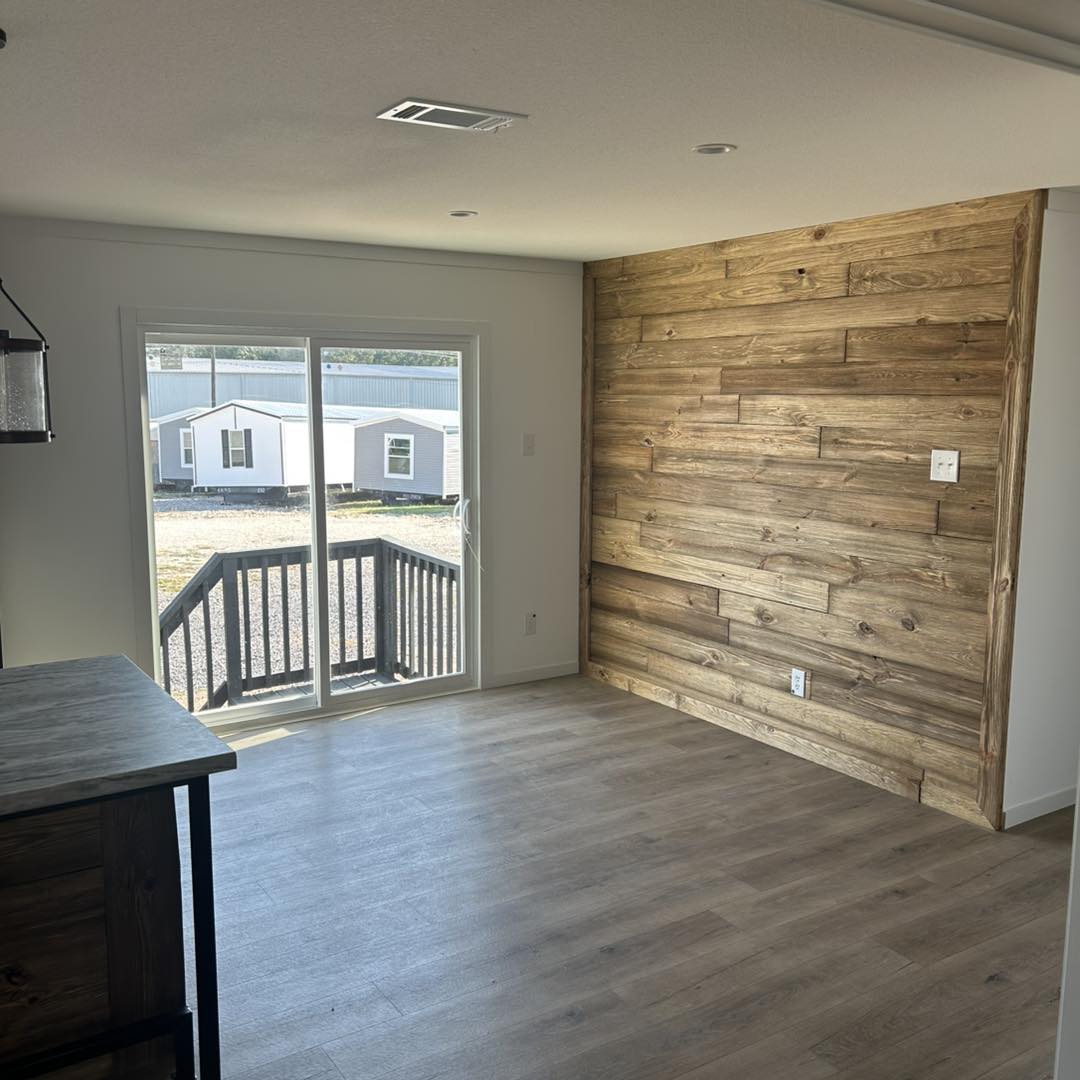 Interior features a wooden accent wall and sliding glass doors leading to a small deck. Natural light fills the space, highlighting the wood flooring.