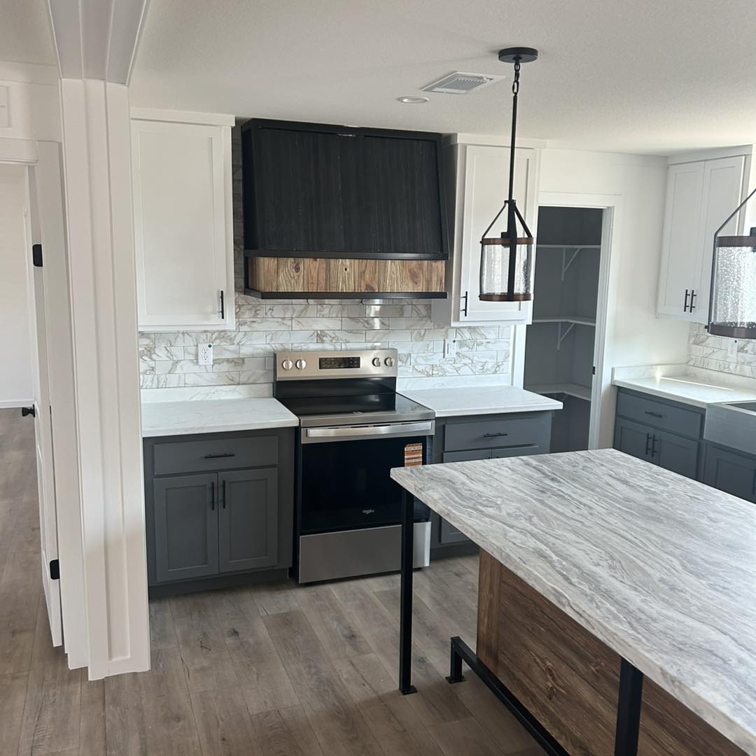 Modern kitchen with white and gray cabinets, wood accents, and marble countertops. Stainless steel stove, pendant lights, and a spacious island.