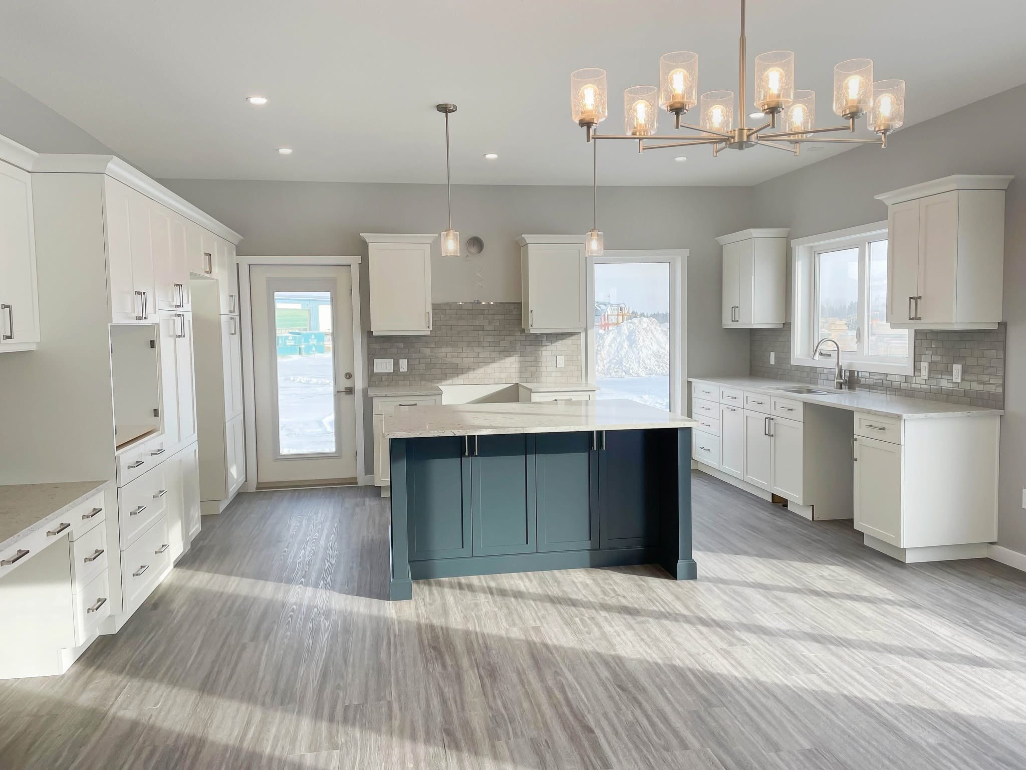 Spacious modern kitchen with white cabinets, gray tile backsplash, and a large navy island. Pendant lighting enhances the sleek, bright space.
