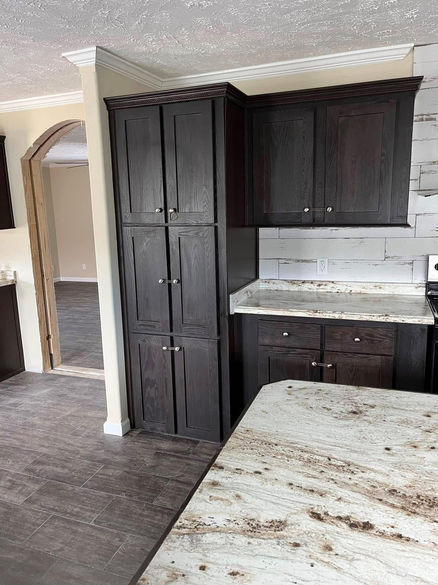 Elegant kitchen with dark wood cabinets, marble countertops, and a tiled backsplash. An archway leads to an adjacent room with wooden floors.