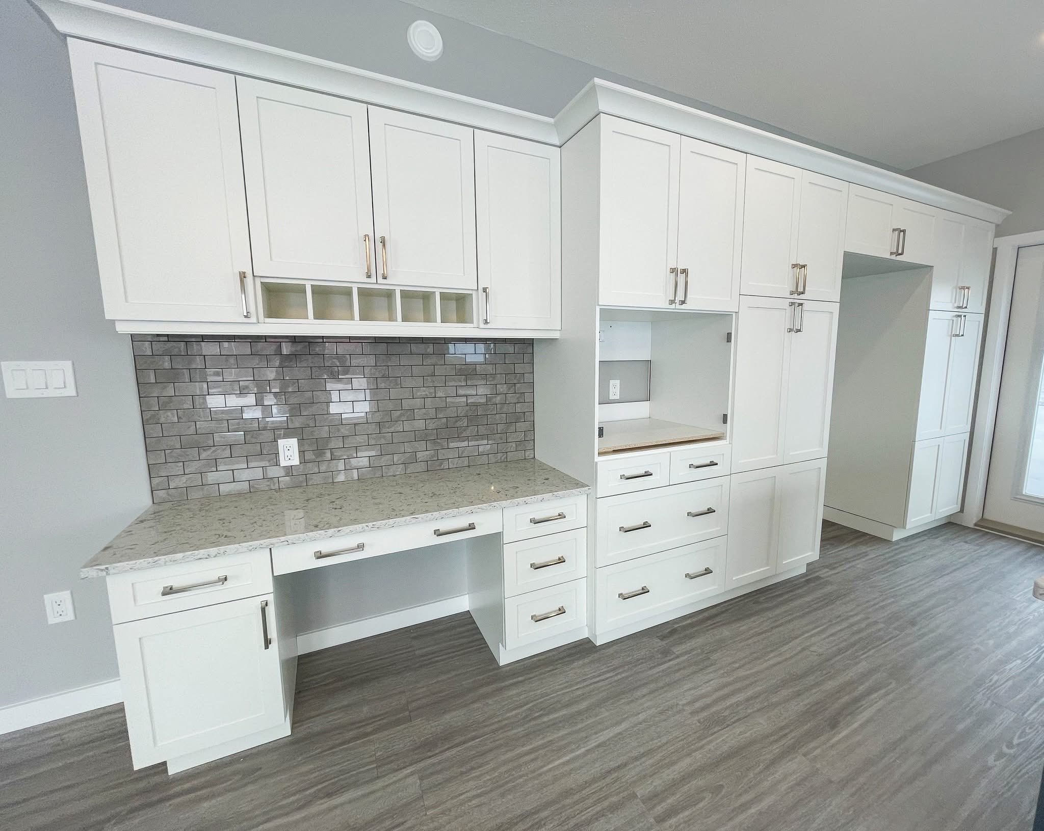 Spacious room with white cabinets and drawers, a gray tile backsplash, and marble countertop, on gray wood flooring, conveying a modern feel.