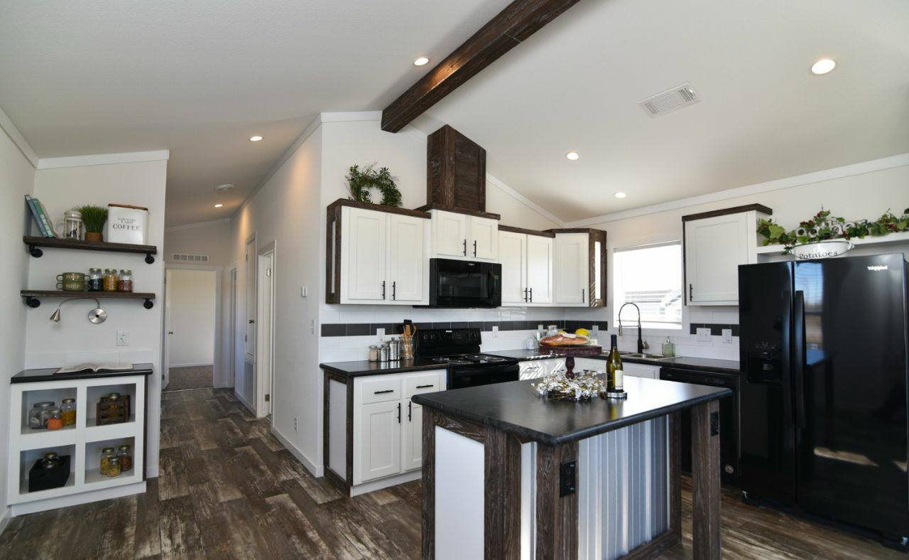 Modern kitchen with white cabinets, dark wood accents, and a black refrigerator. Central island with a black countertop, wine bottle, and grapes. Cozy and inviting.