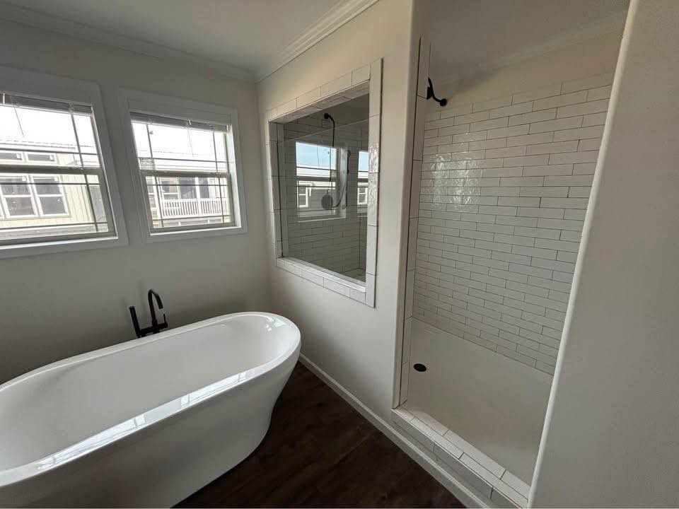 Modern bathroom with a freestanding white tub and black faucet on a dark floor. Adjacent is a walk-in shower with white subway tiles, exuding a clean, minimalist style.