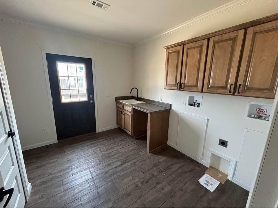 Laundry room with wood cabinets and a sink on the right, dark wood floor, and a black door with glass panes on the left, creating a functional and inviting space.