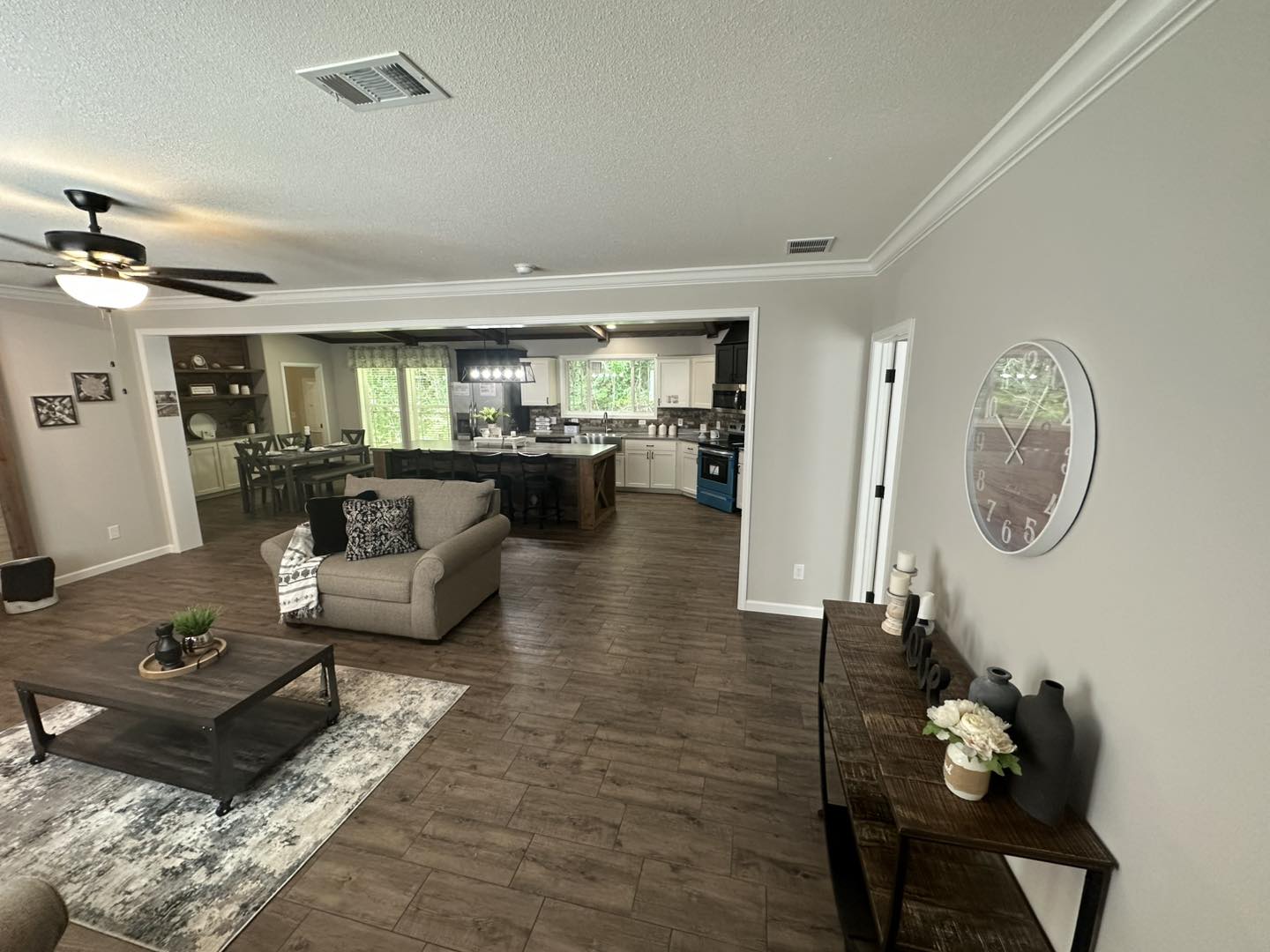 Spacious open-plan living room and kitchen with wood floors. A large sofa, coffee table, and wall clock create a cozy, modern ambiance.