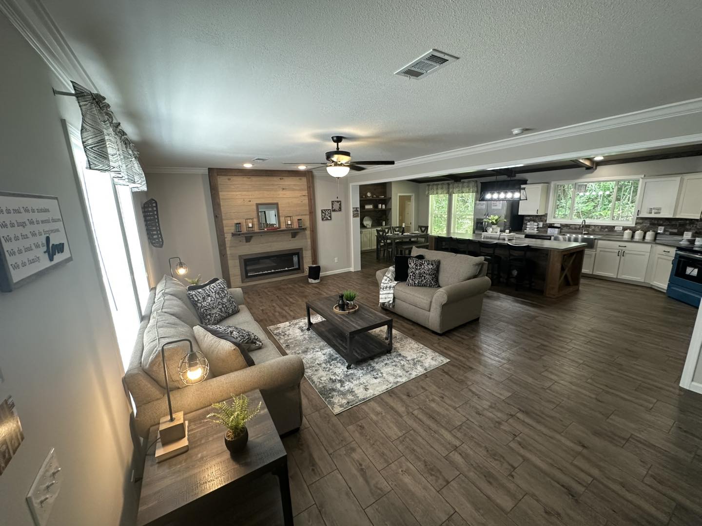 Spacious, modern living room with neutral tones, cozy sofa, coffee table, and fireplace. Open kitchen with bar seating, large windows, and bright lighting.