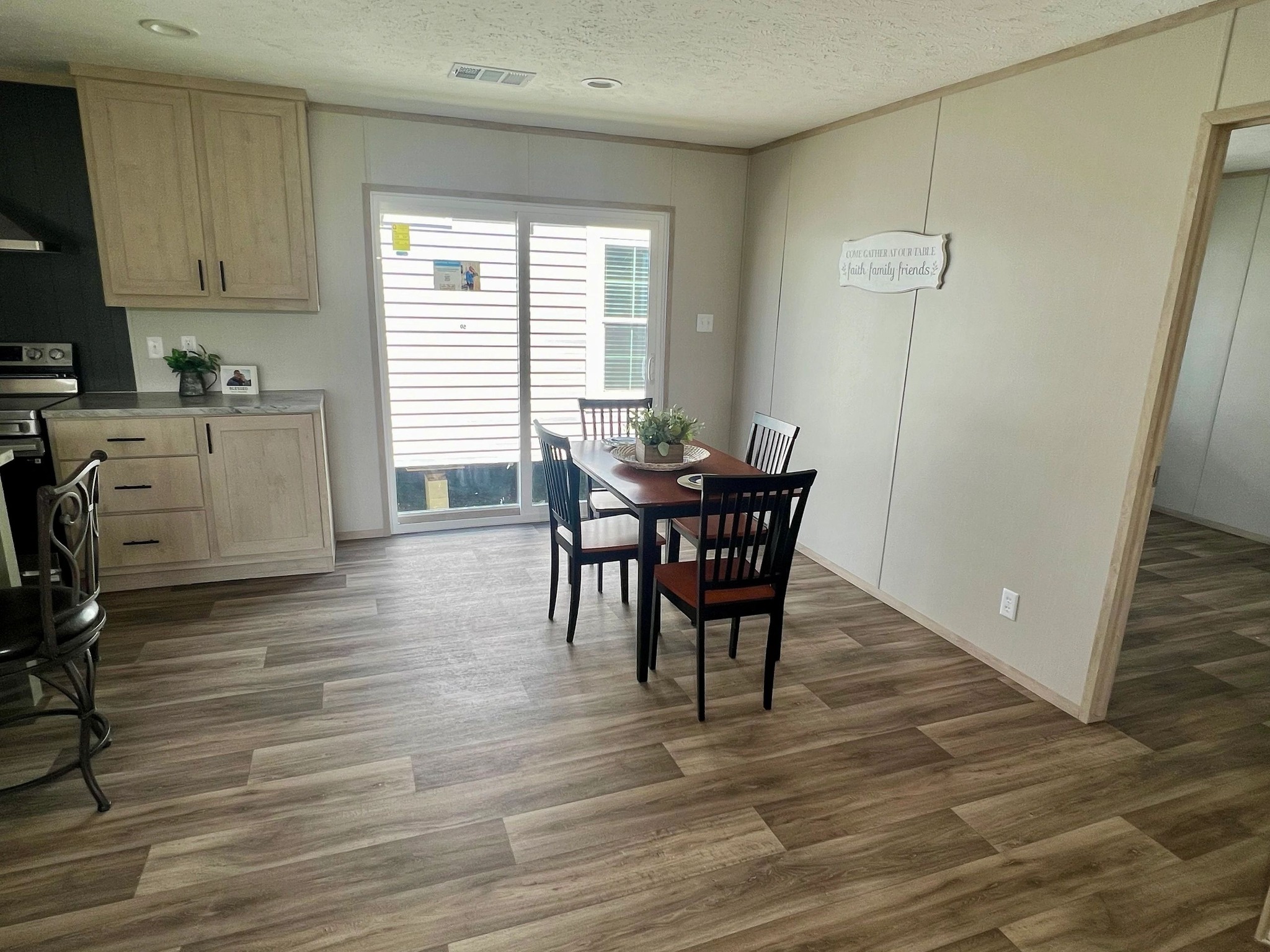 A cozy dining area with wooden floors features a table set for four. Natural light streams in through large sliding doors. Warm and inviting ambiance.