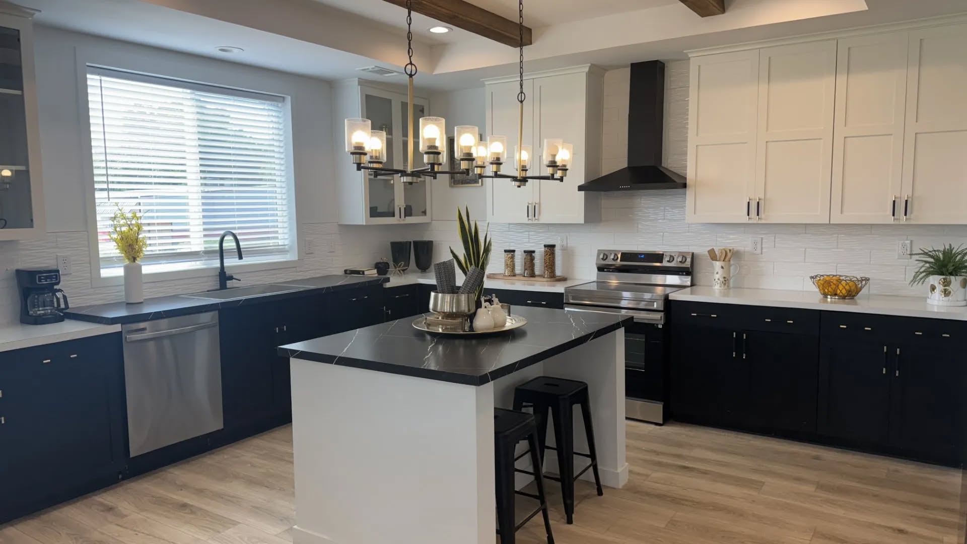 Modern kitchen with black and white cabinetry, center island with stools, stainless steel appliances, and a chandelier. Bright and welcoming atmosphere.