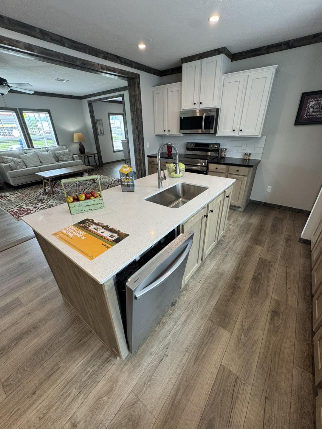 Modern kitchen with white cabinets, stainless steel appliances, center island with sink, and barstool. Adjacent cozy living room with sofa and lamp.