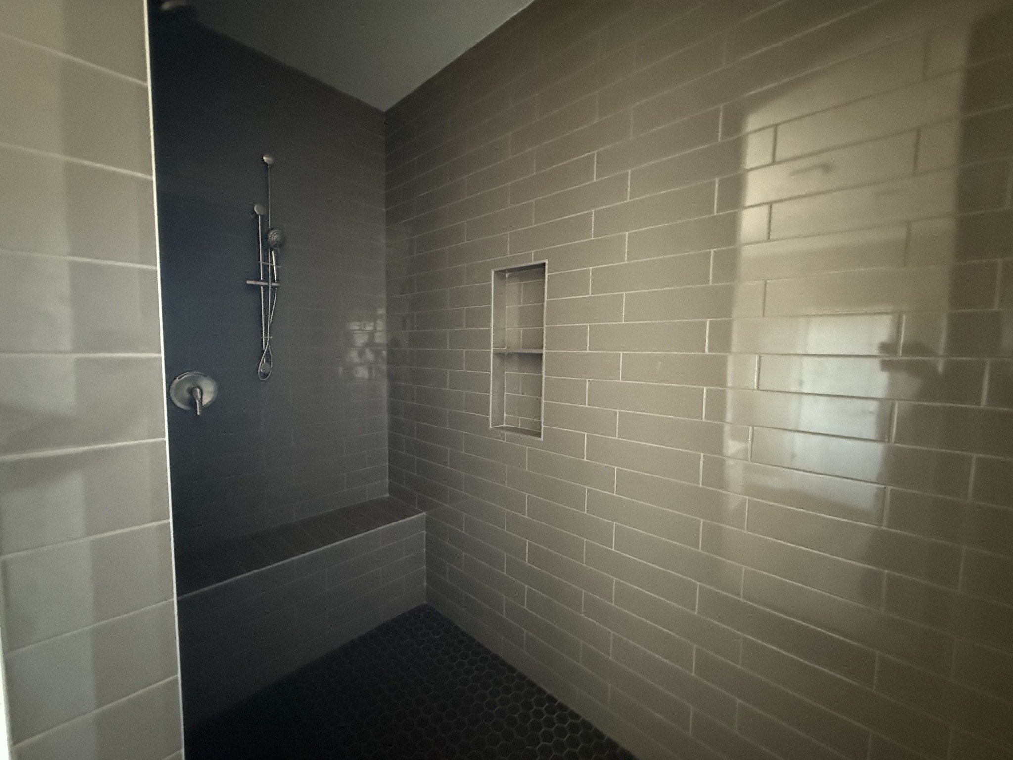 A modern shower with beige subway tiles, a built-in bench, and a recessed shelf. The space is clean and minimalistic, conveying a calm, serene mood.