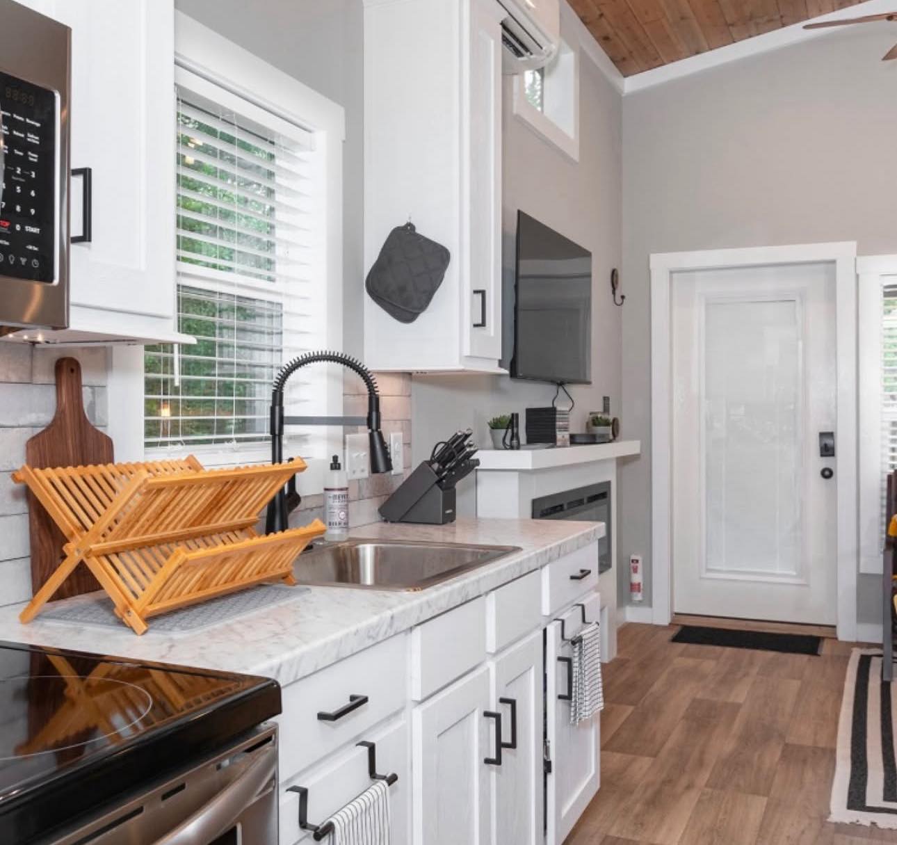 Modern kitchen with white cabinets, marble countertops, and a black faucet. A wooden dish rack sits beside a knife set. The room has a warm, inviting feel.