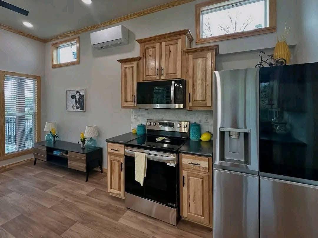 Modern kitchen with stainless steel appliances, light wood cabinets, and dark countertops. Bright, airy atmosphere with natural light from windows. Cozy and inviting.