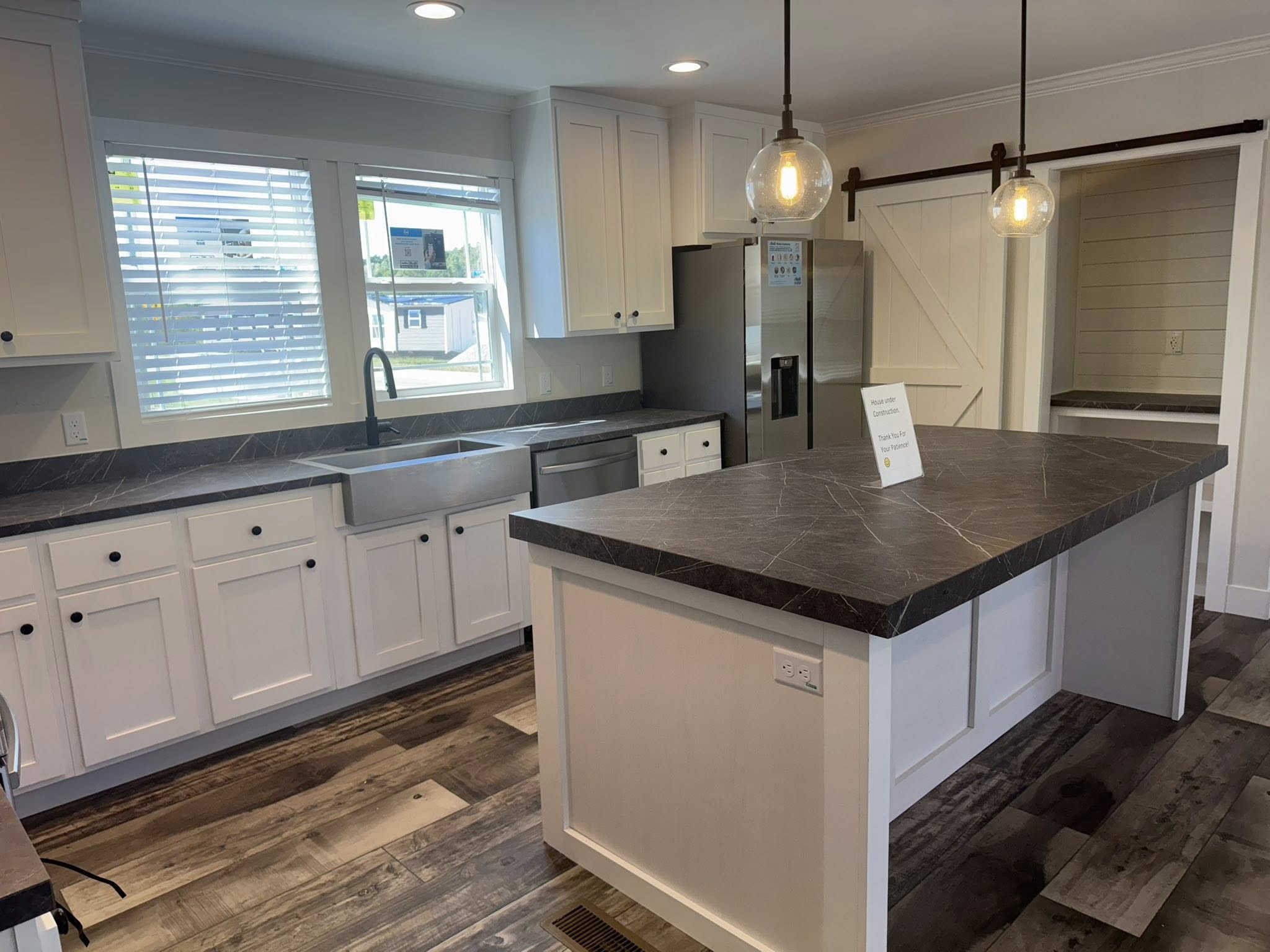 Modern kitchen with white cabinets, dark stone countertops, and wood floors. Large island with pendant lights and a stainless steel farmhouse sink.