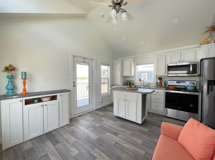 Bright kitchen interior with white cabinets, stainless steel appliances, and an island. French doors, colorful vases, and a peach sofa add vibrancy.