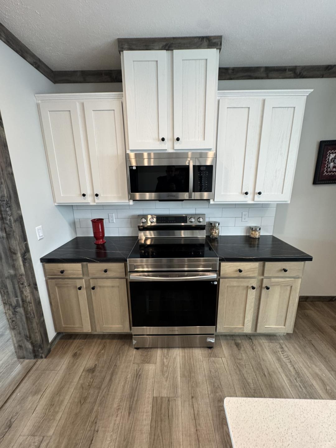 Modern kitchen with white cabinets, stainless steel stove and microwave, and dark countertops. Wooden floor adds warmth, evoking a clean, cozy vibe.