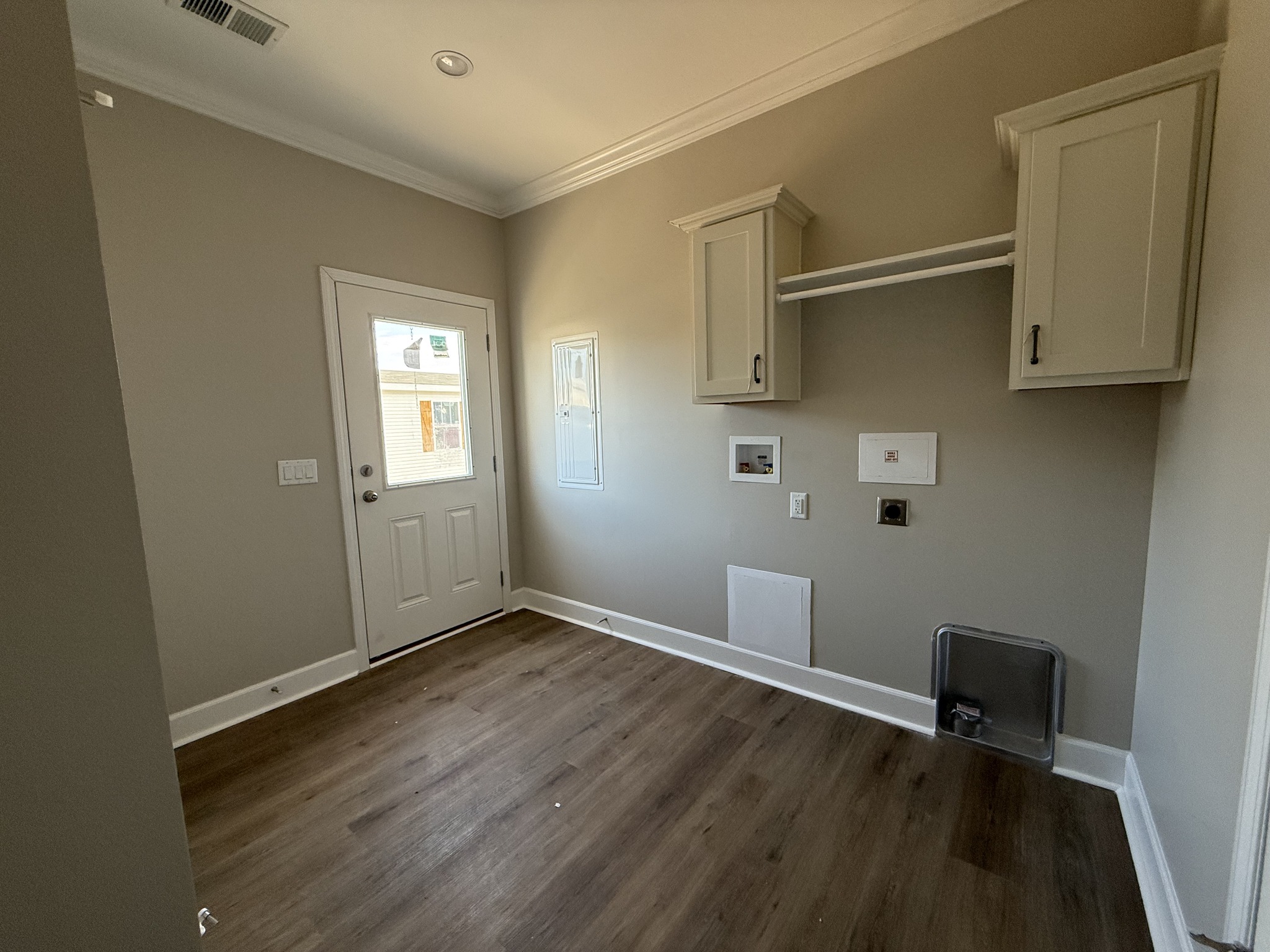 Empty laundry room with beige walls, wooden floor, white door, and two wall cabinets. Space conveys a clean and minimalist vibe.