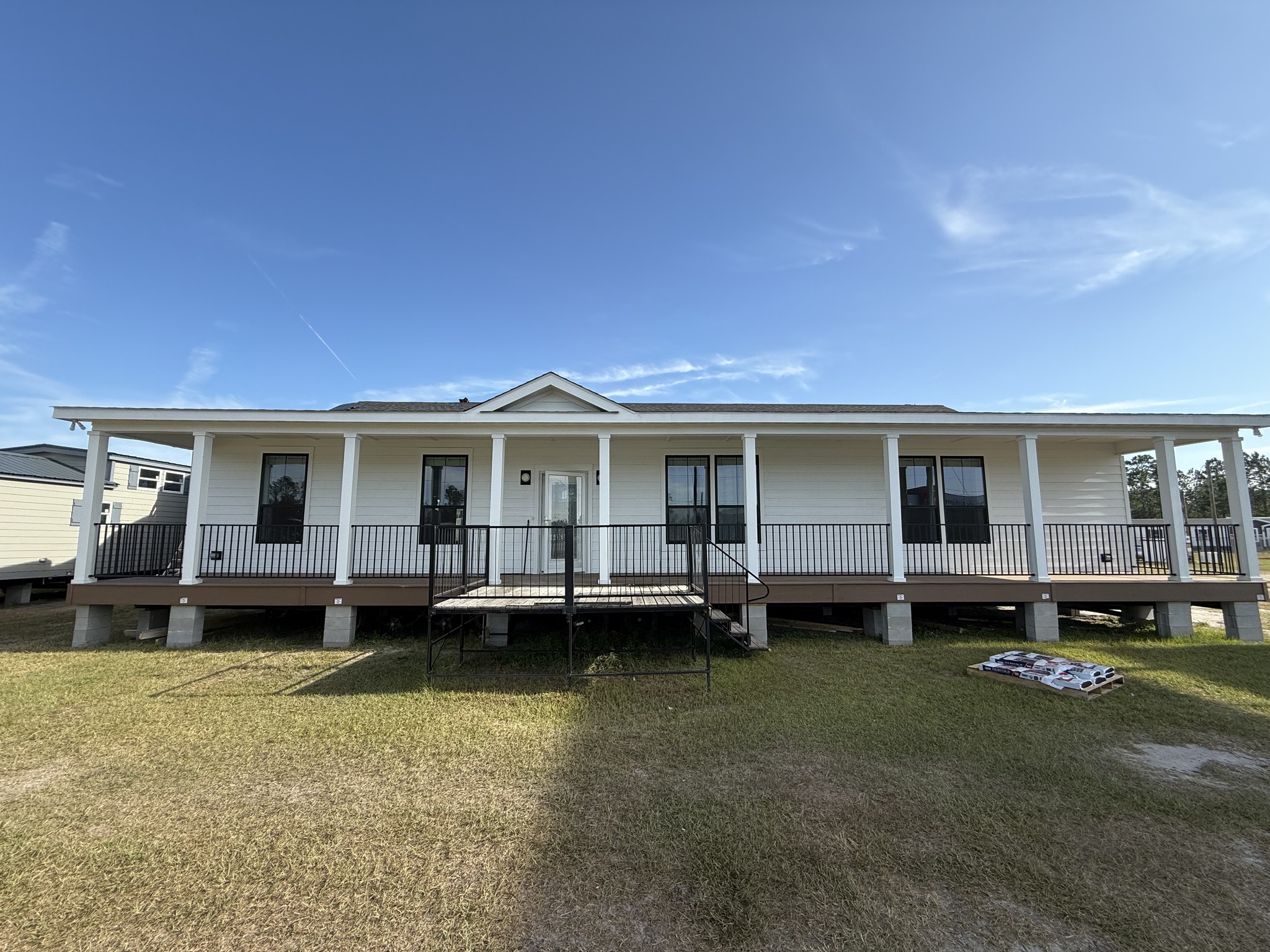 Single-story white house with a wide front porch and black railings, set on a grassy lawn under a clear blue sky. Calm and spacious atmosphere.