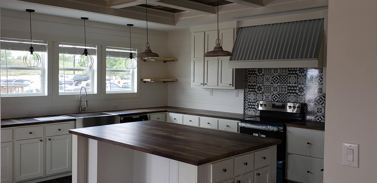 Bright kitchen with white cabinets and dark wood countertops. Features a patterned tile backsplash, large island, and pendant lights, creating a modern, inviting atmosphere.