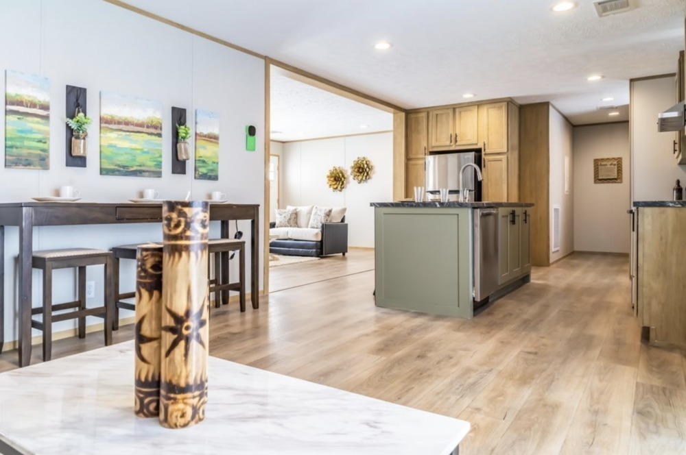 Modern open-concept kitchen and dining area with wooden floors. Features a central island, dining table with stools, wall art, and cozy living space.