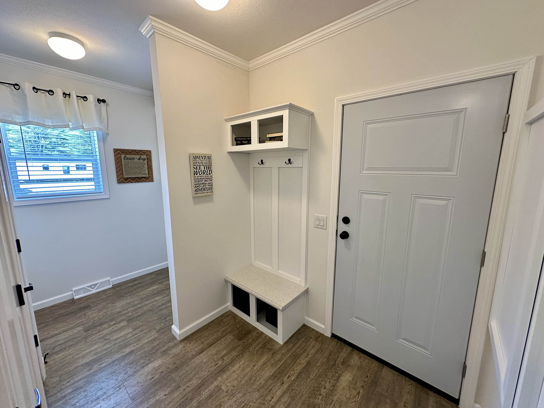 A small entryway with a light gray door and wooden flooring. Features a white hall tree with hooks and storage, conveying an organized, welcoming space.