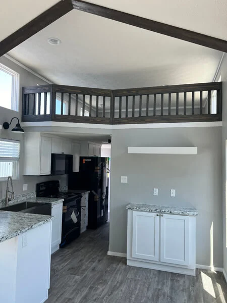 Modern kitchen with white cabinets, granite countertops, and dark appliances. Loft area with a wooden railing above adds spaciousness and style.
