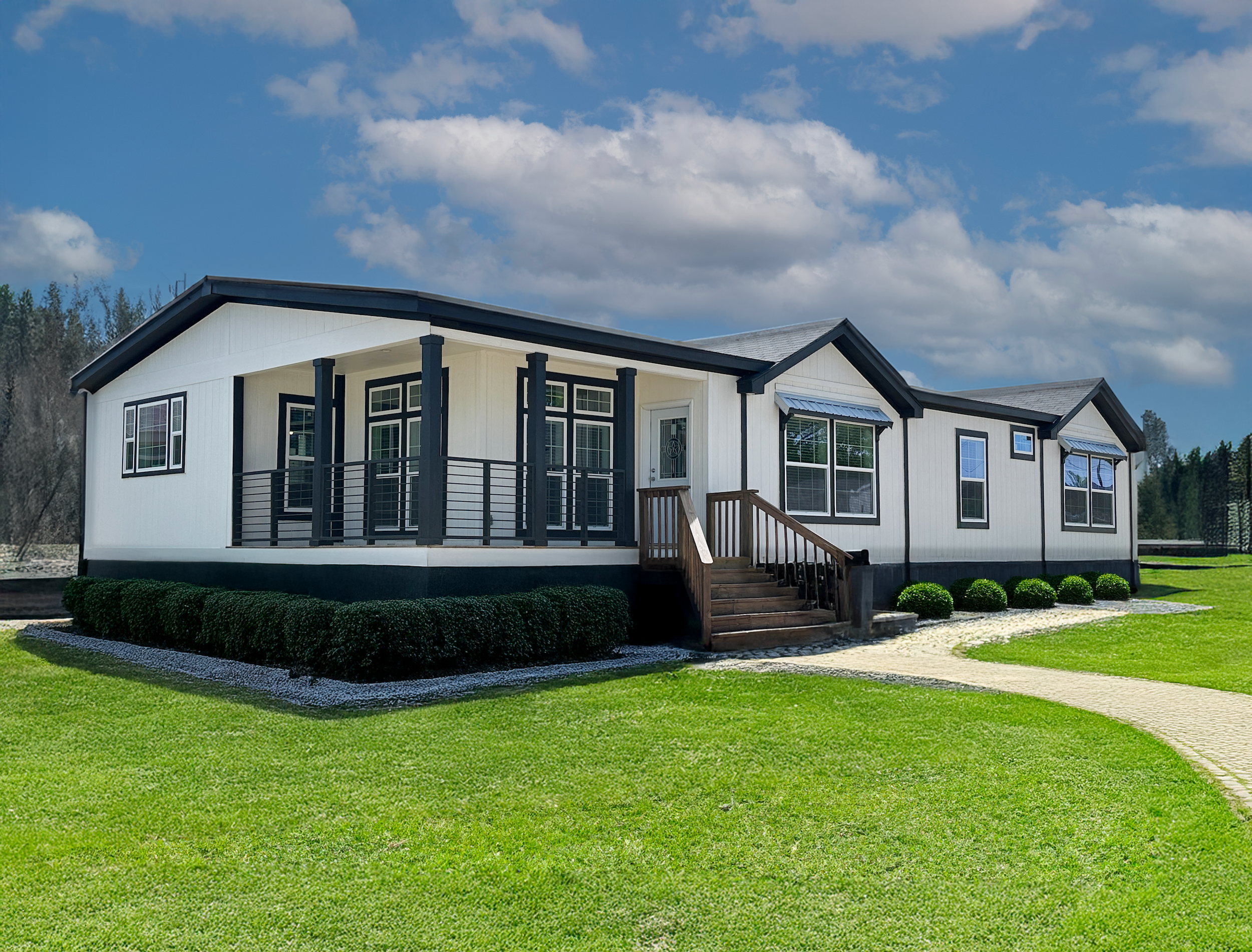 A modern, single-story modular home with white siding and dark trim, set against a vibrant green lawn, under a partly cloudy blue sky.