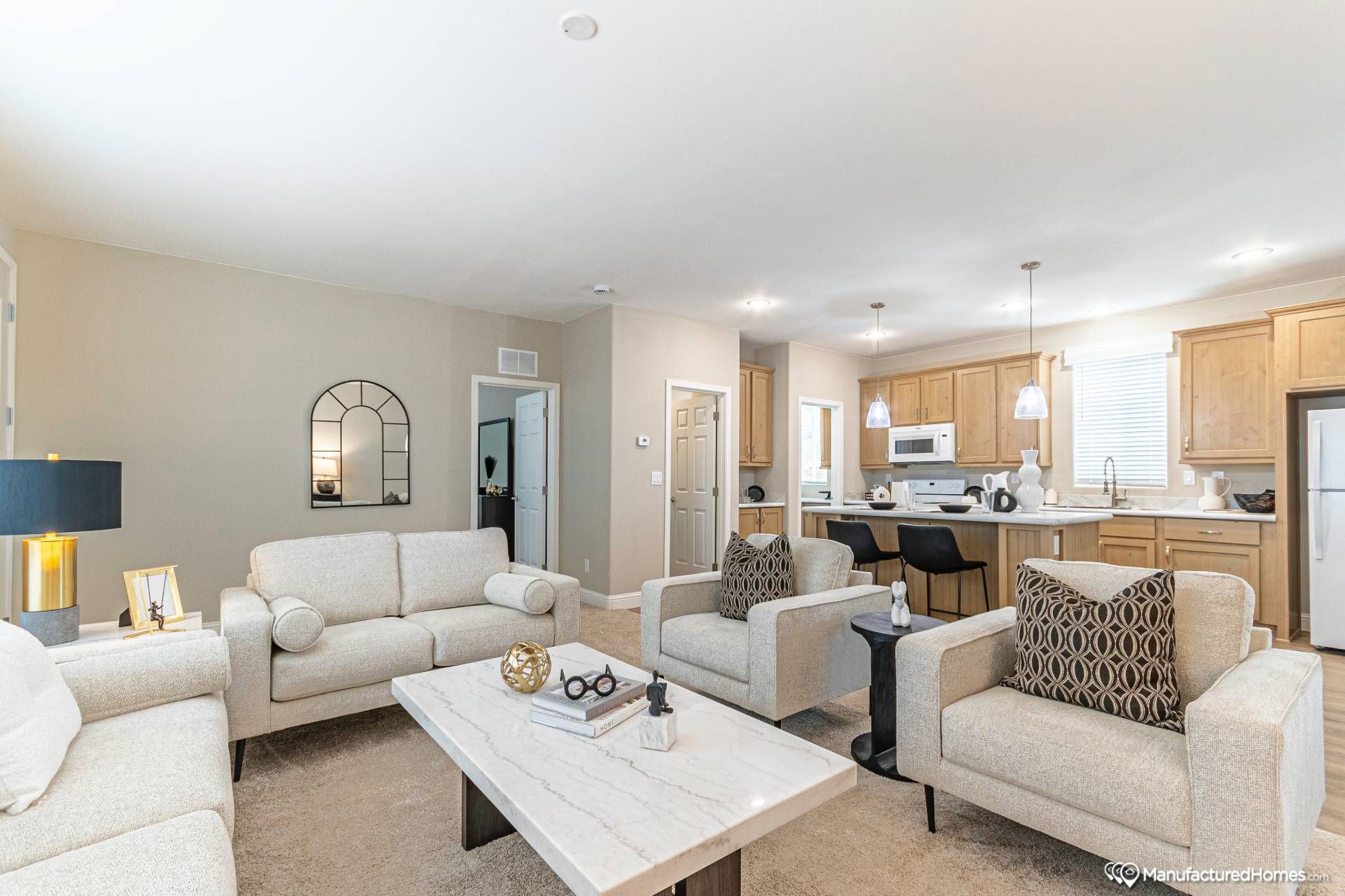 Modern living room with beige sofas and armchairs arranged around a marble coffee table. Open kitchen with warm wooden cabinets in the background. Cozy and inviting atmosphere.