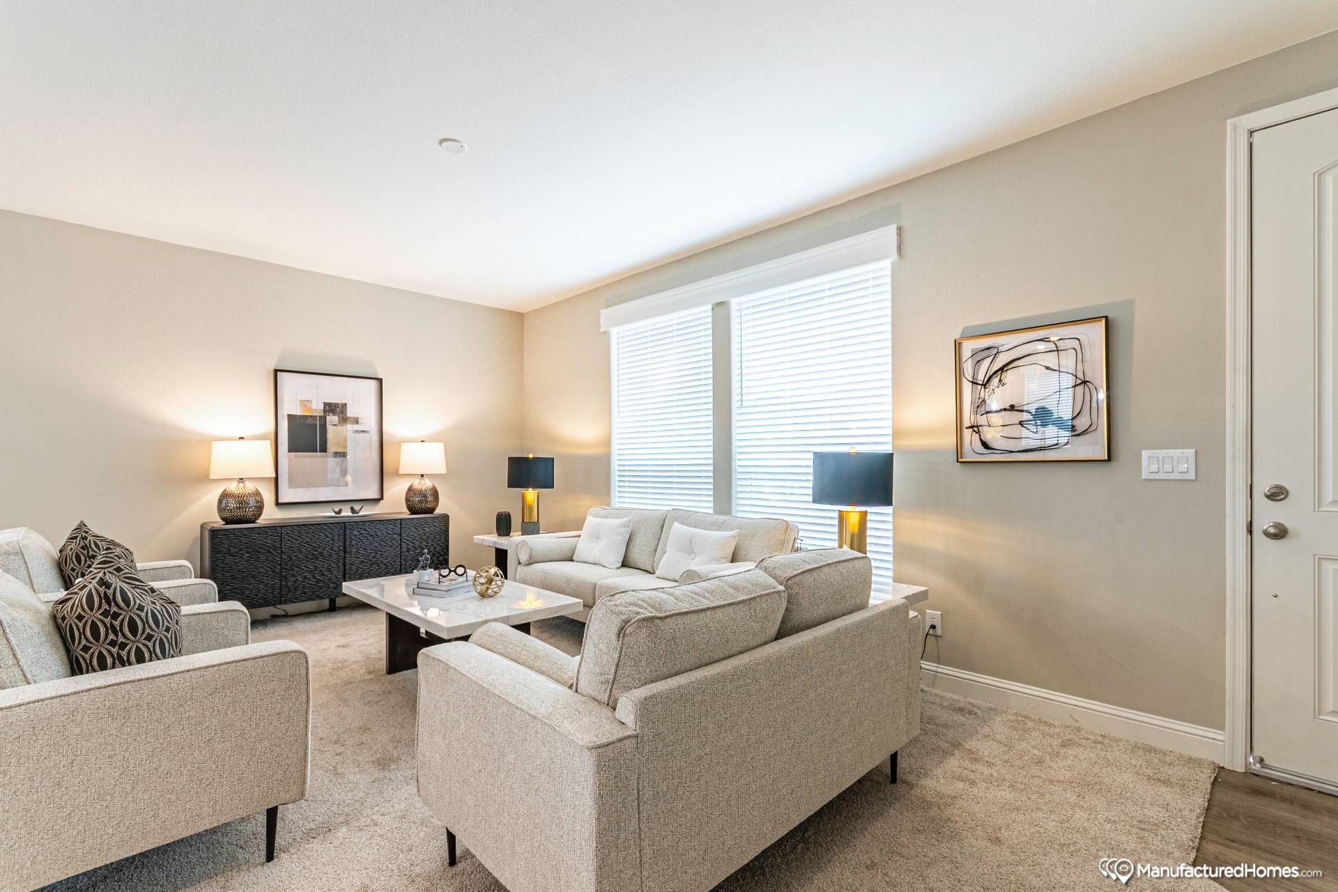 Modern living room with beige sofas, a marble coffee table, and black lamps. Abstract art and natural light create a cozy, elegant ambiance.