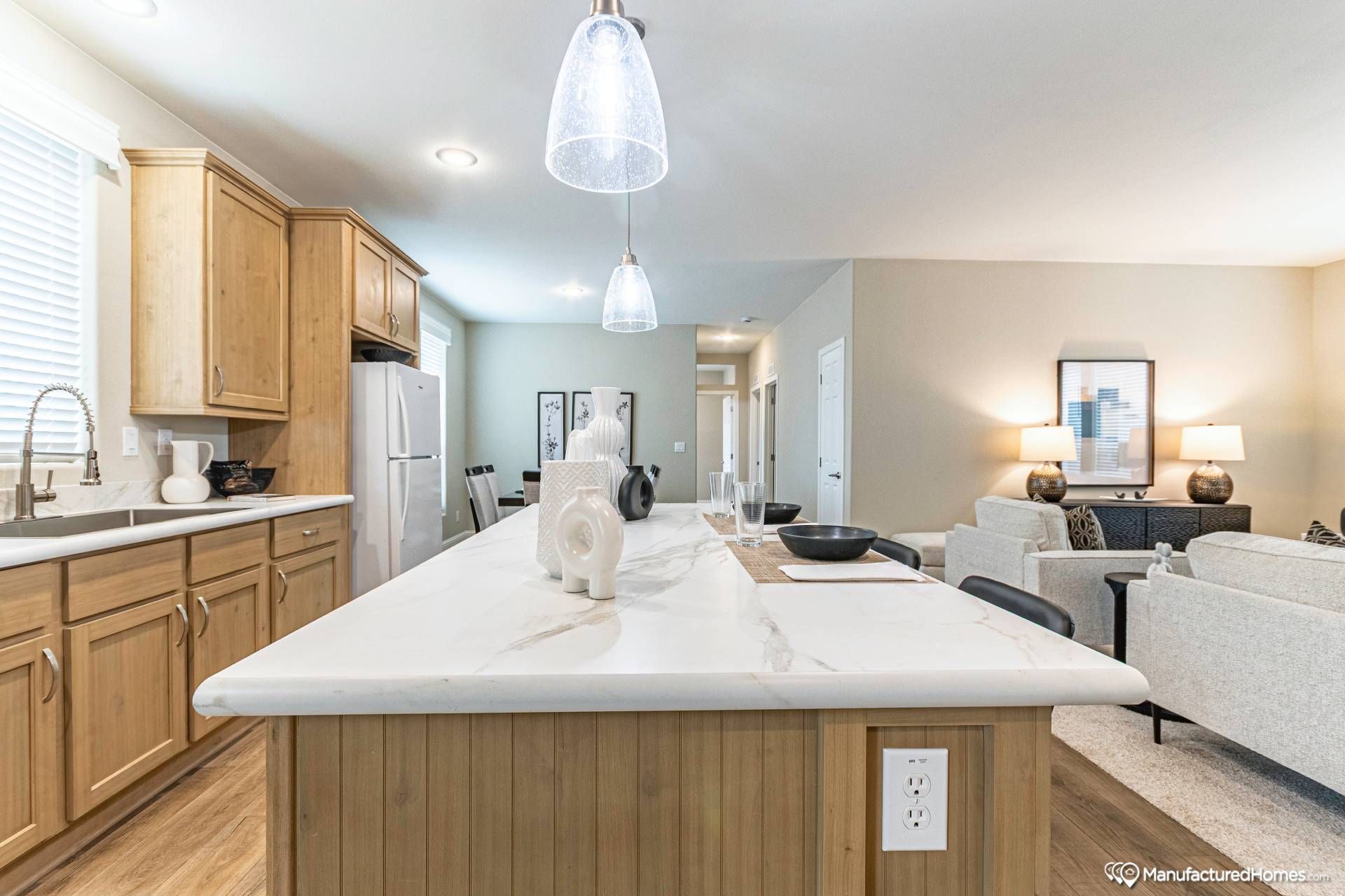 Modern kitchen and living area with wooden cabinets, a marble island, and pendant lighting. Cozy seating area with neutral tones and warm lighting.
