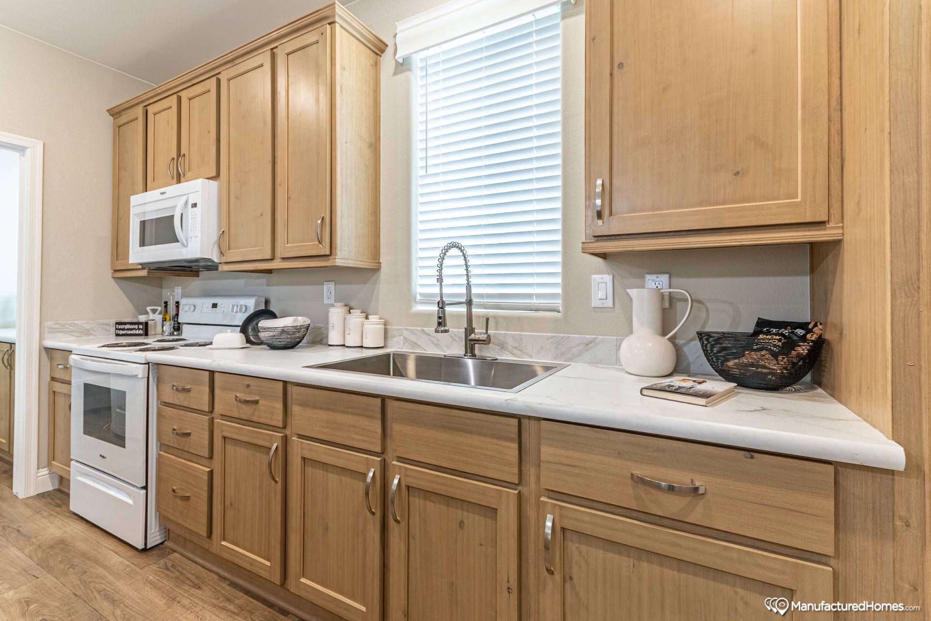 Modern kitchen with wooden cabinets, white marble countertops, a stainless steel sink, and a white stove and microwave. Bright and organized.
