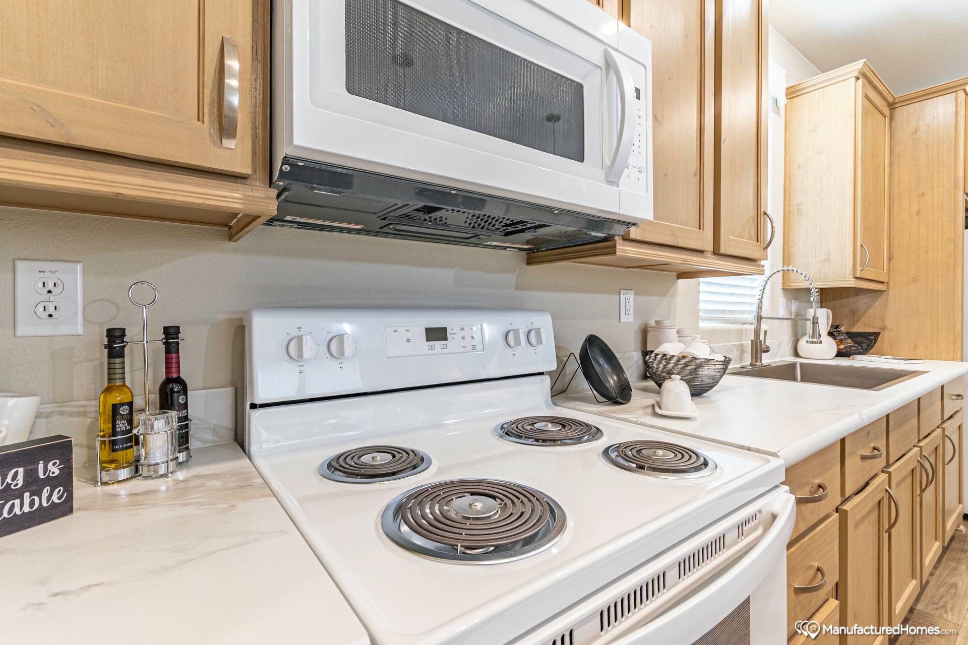 Modern kitchen with white stove and overhead microwave, wooden cabinets, and a marble countertop. Accessories include oil bottles and a sink. Cozy ambiance.