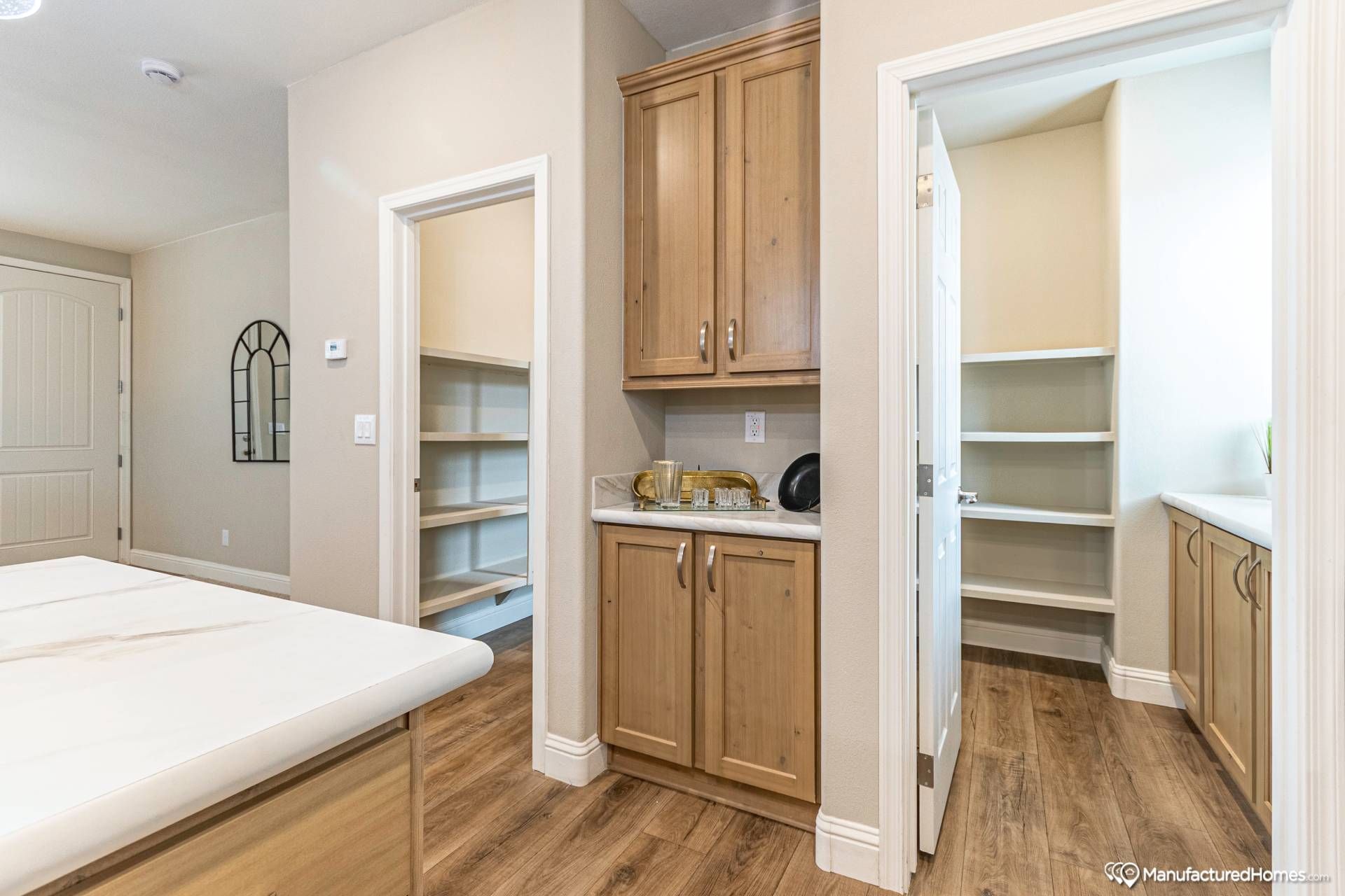 Bright kitchen with light wooden cabinets, white countertops, and open pantry shelves. Warm wood flooring adds a cozy ambiance. Simple, modern design.