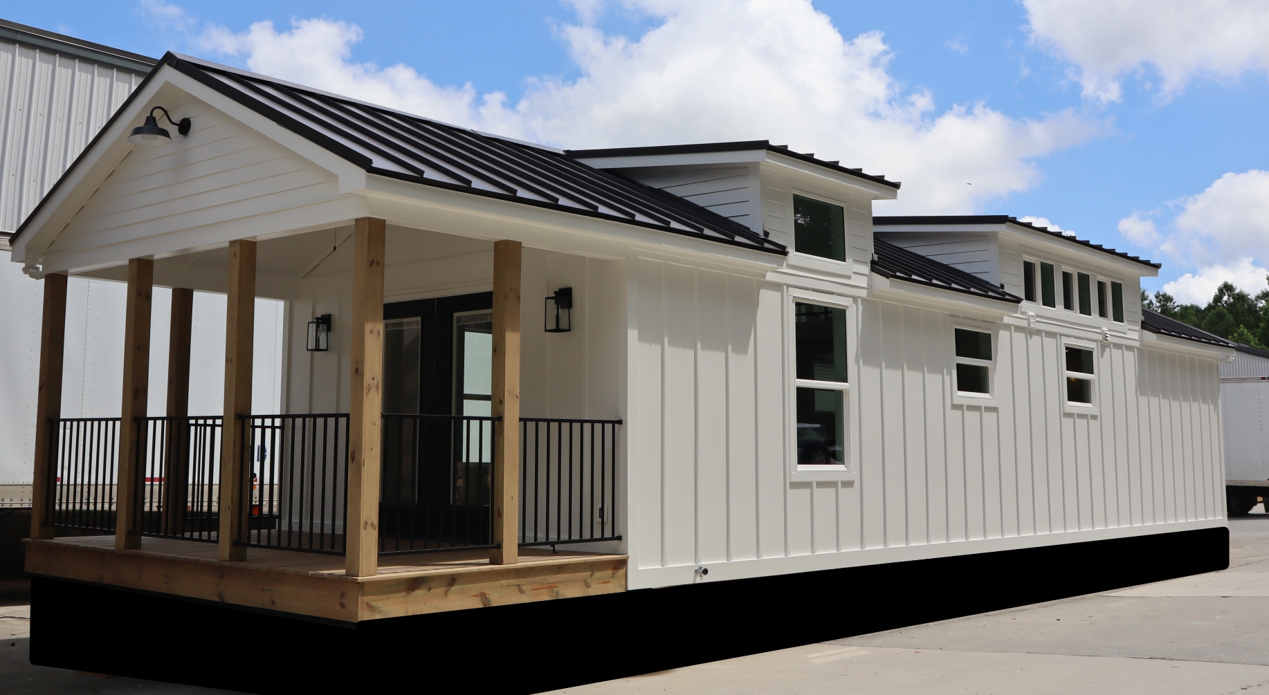 A modern tiny house with white siding, black metal roof, and wooden porch. Large windows and clean lines evoke a minimalist and cozy feel on a sunny day.