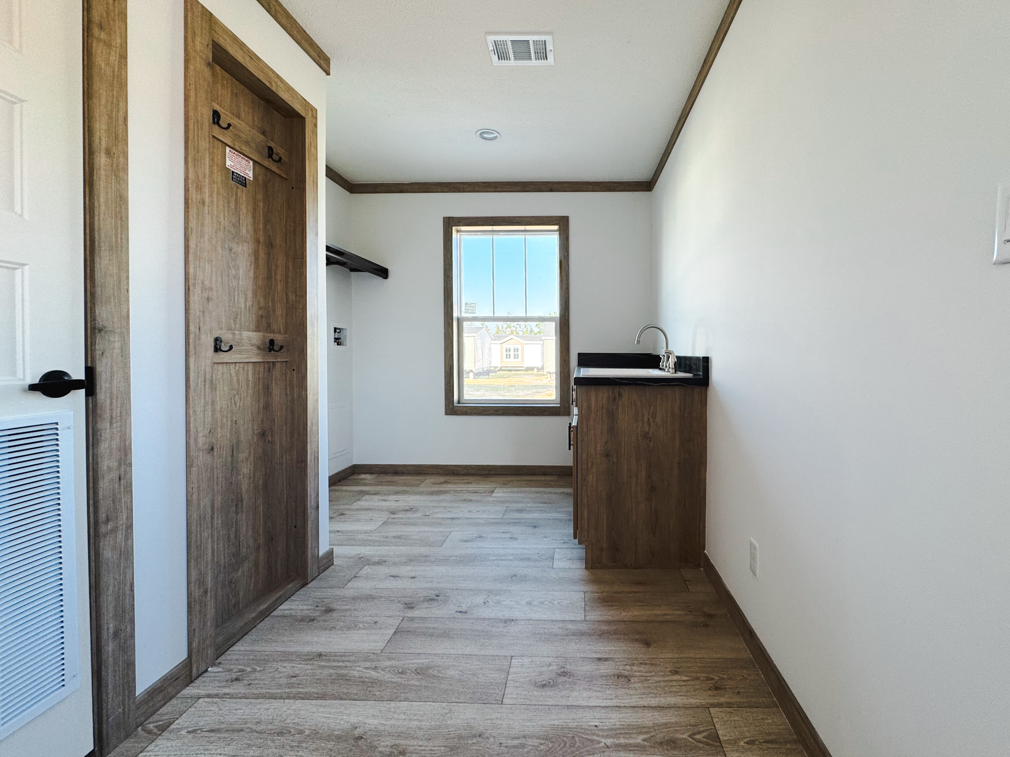 Compact room with wooden floors and trim, featuring a small window, a closed door, and a kitchenette with a black countertop. Bright and minimalist.
